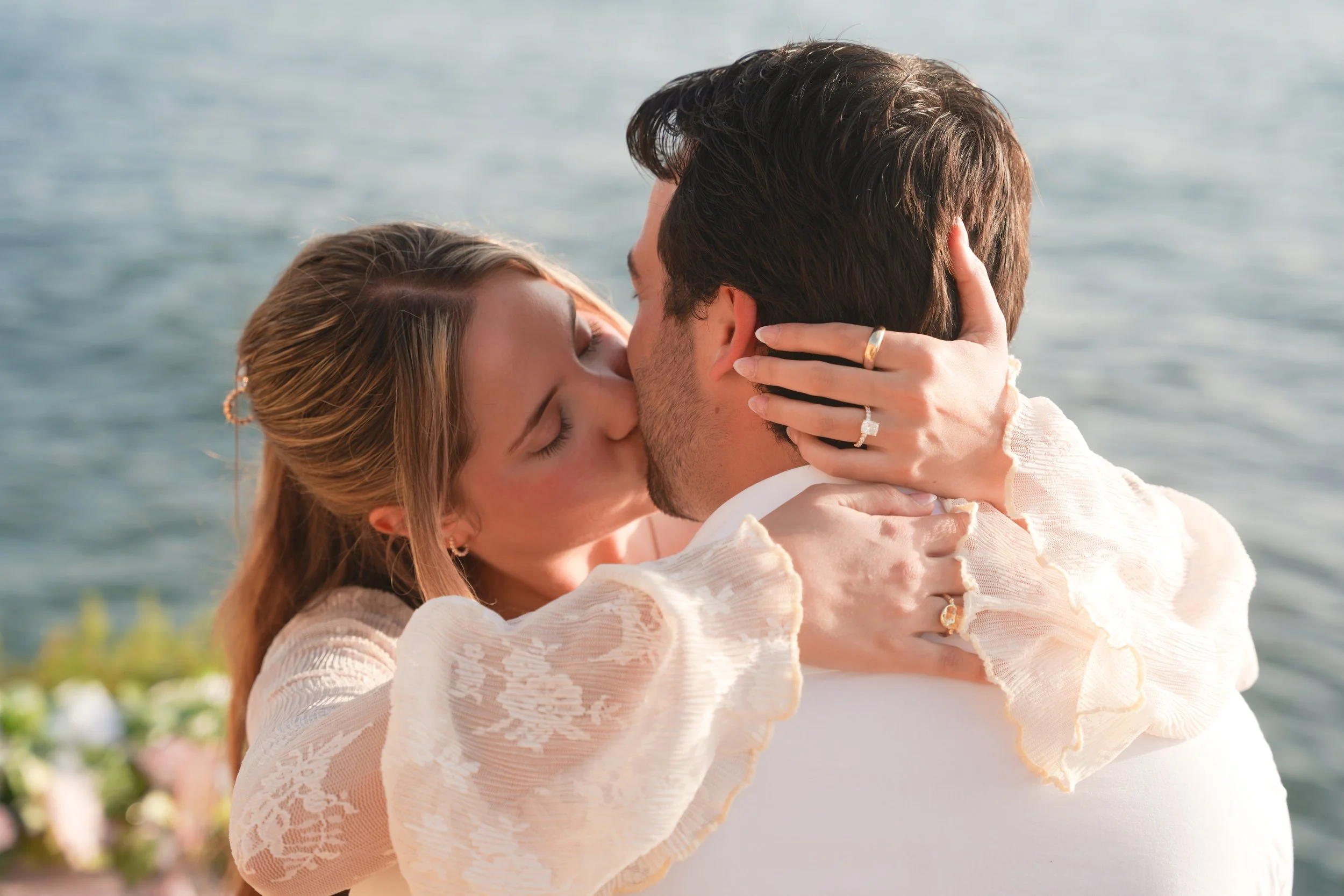 Fiancée kissing her partner moments after a surprise proposal at a luxury cliffside picnic, captured by a professional surprise proposal photographer in San Diego with ocean sunset backdrop