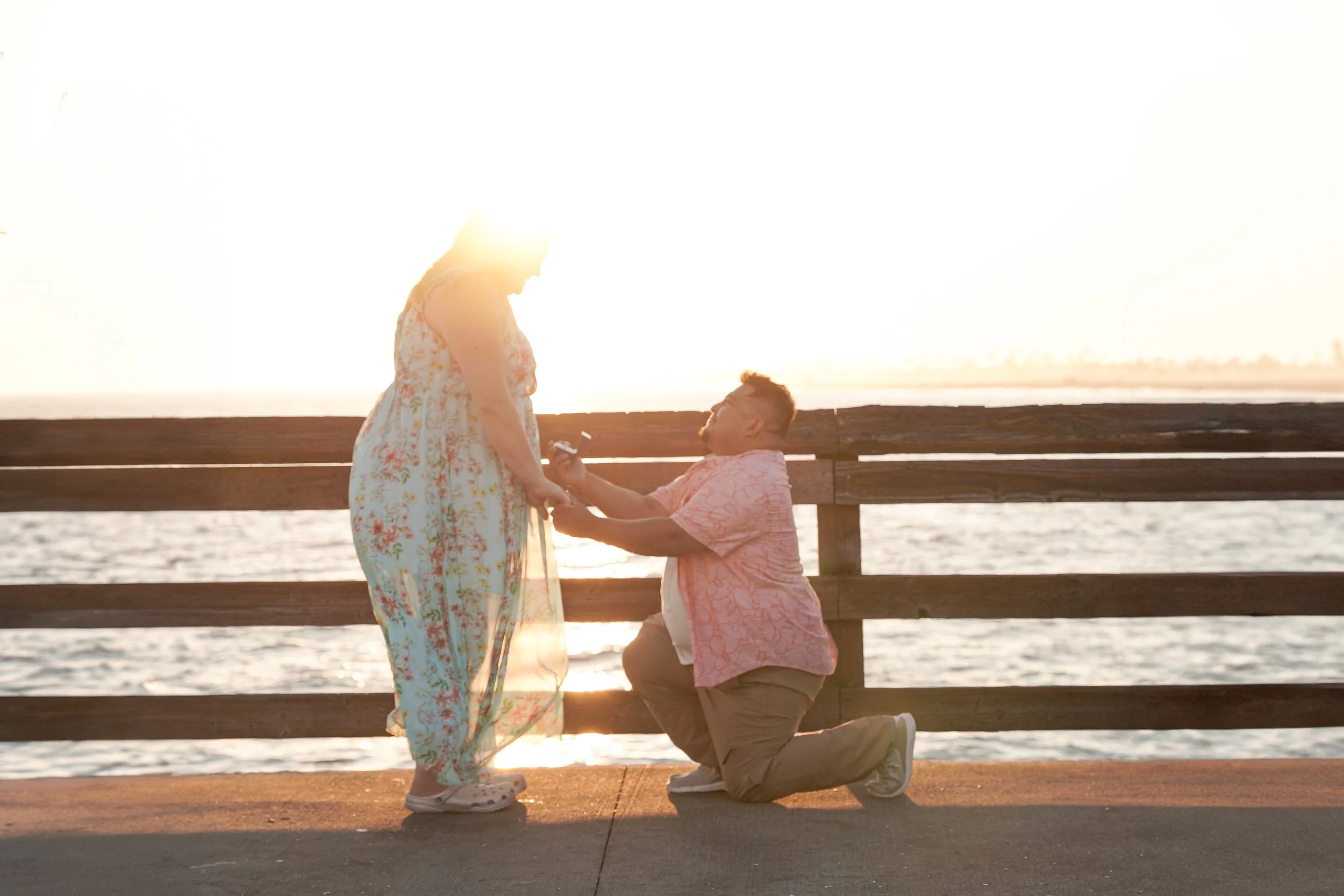 Orange County proposal photography at Balboa Pier in Newport Beach with Miguel down on one knee, Jennifer says yes in emotional engagement.