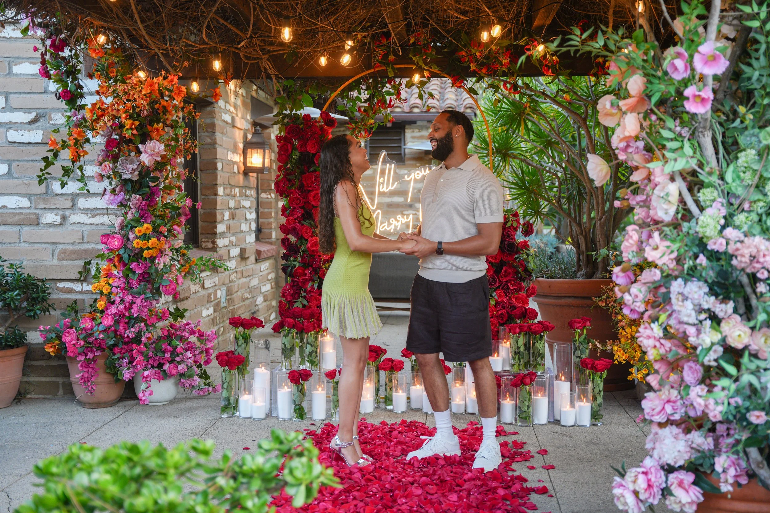 David placing an engagement ring on Leila's finger during their surprise proposal at Estancia La Jolla.