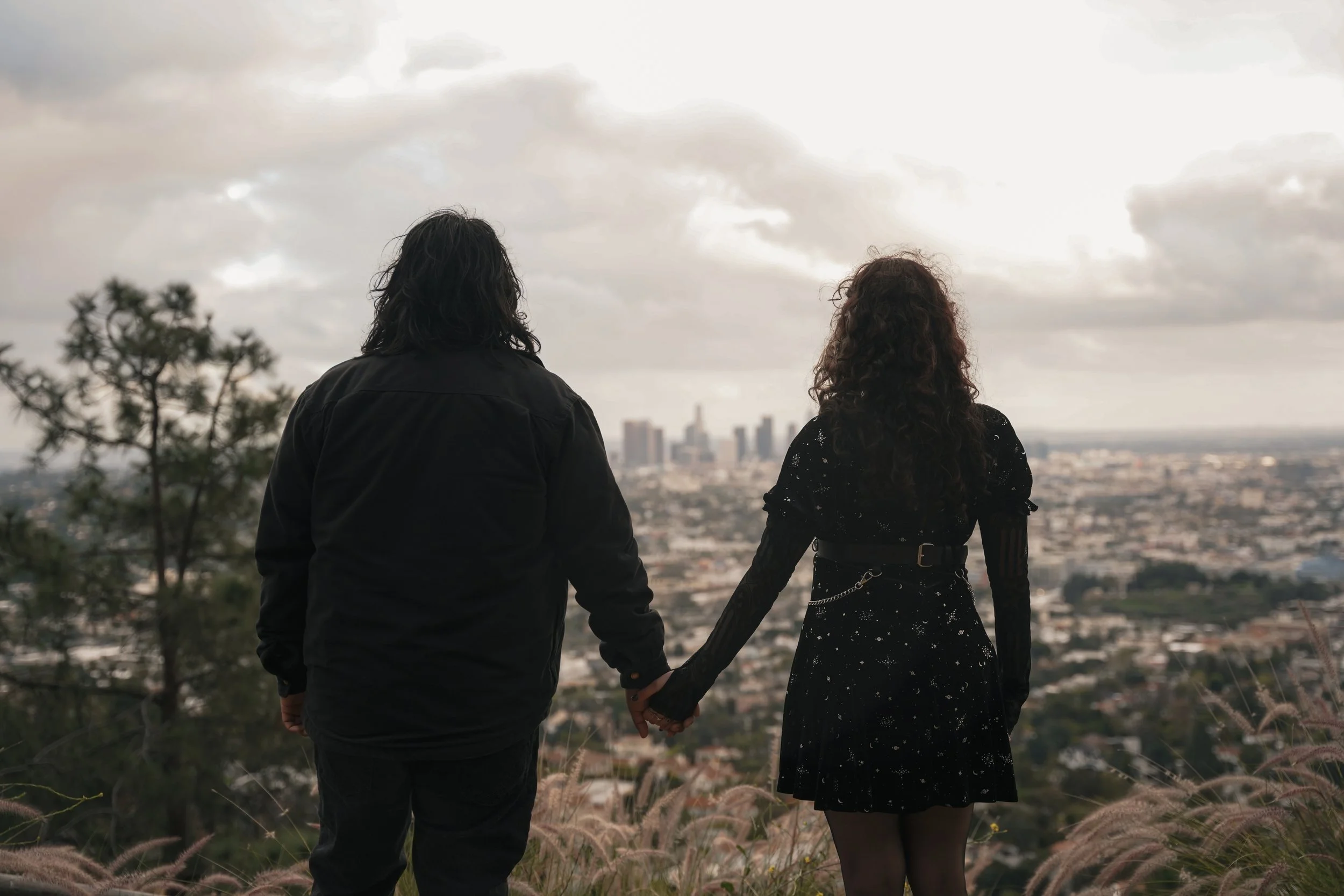 Recently engaged couple standing on the trails beside Griffith Observatory overlooking the Downtown Los Angeles skyline after their surprise proposal.