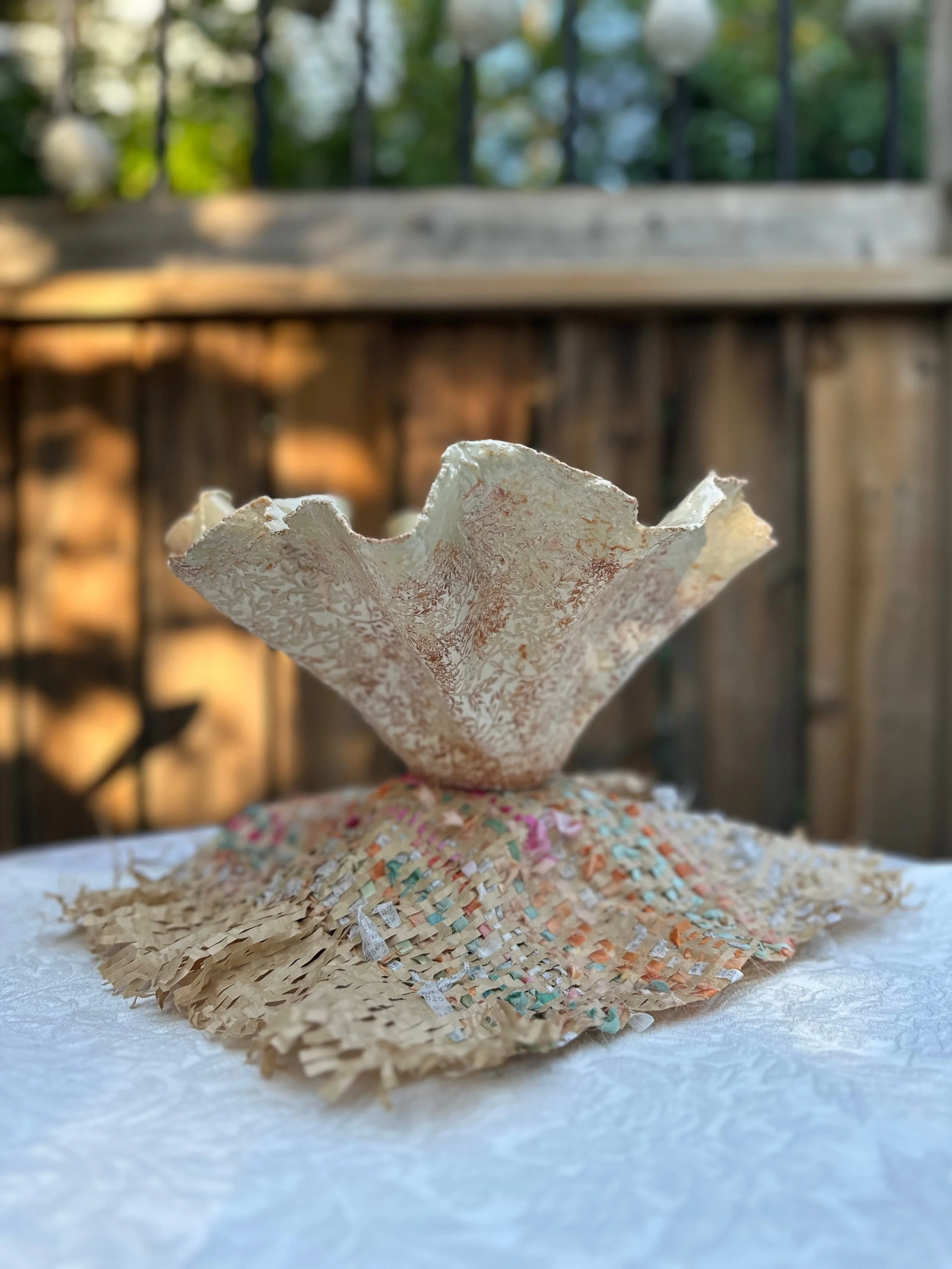 A fold-vessel bowl sculpture rests on a woven paper mound, in the sun of late afternoon.