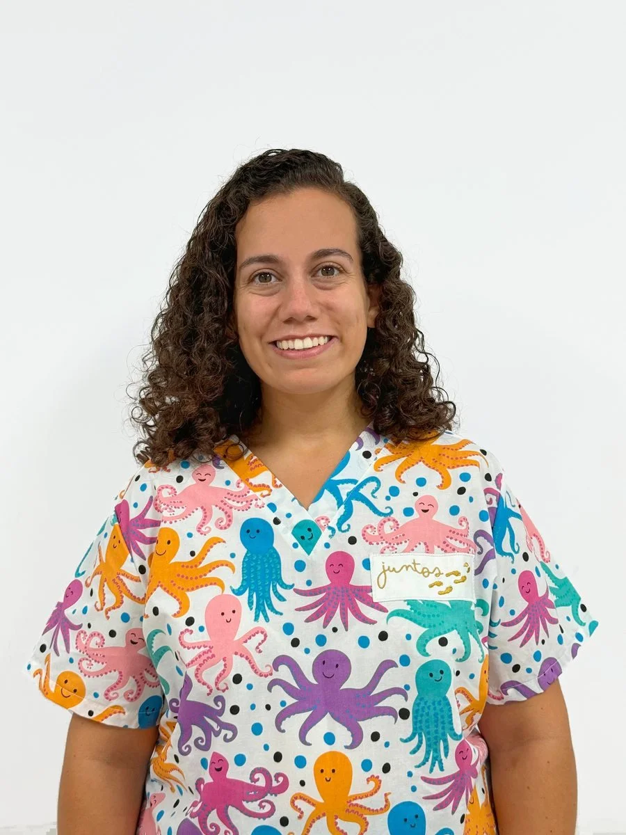 Mujer con cabello rizado, sonriendo, usando uniforme con pulpos de colores en fondo blanco.