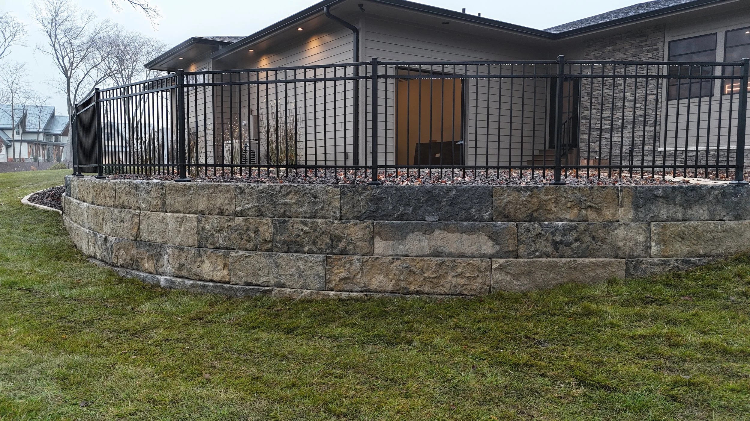 Stone retaining wall with black metal fence in backyard of a modern house.