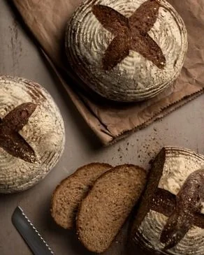 Dark and hearty grain bread boules placed on a kraft bag with some sliced pieces and crumbs