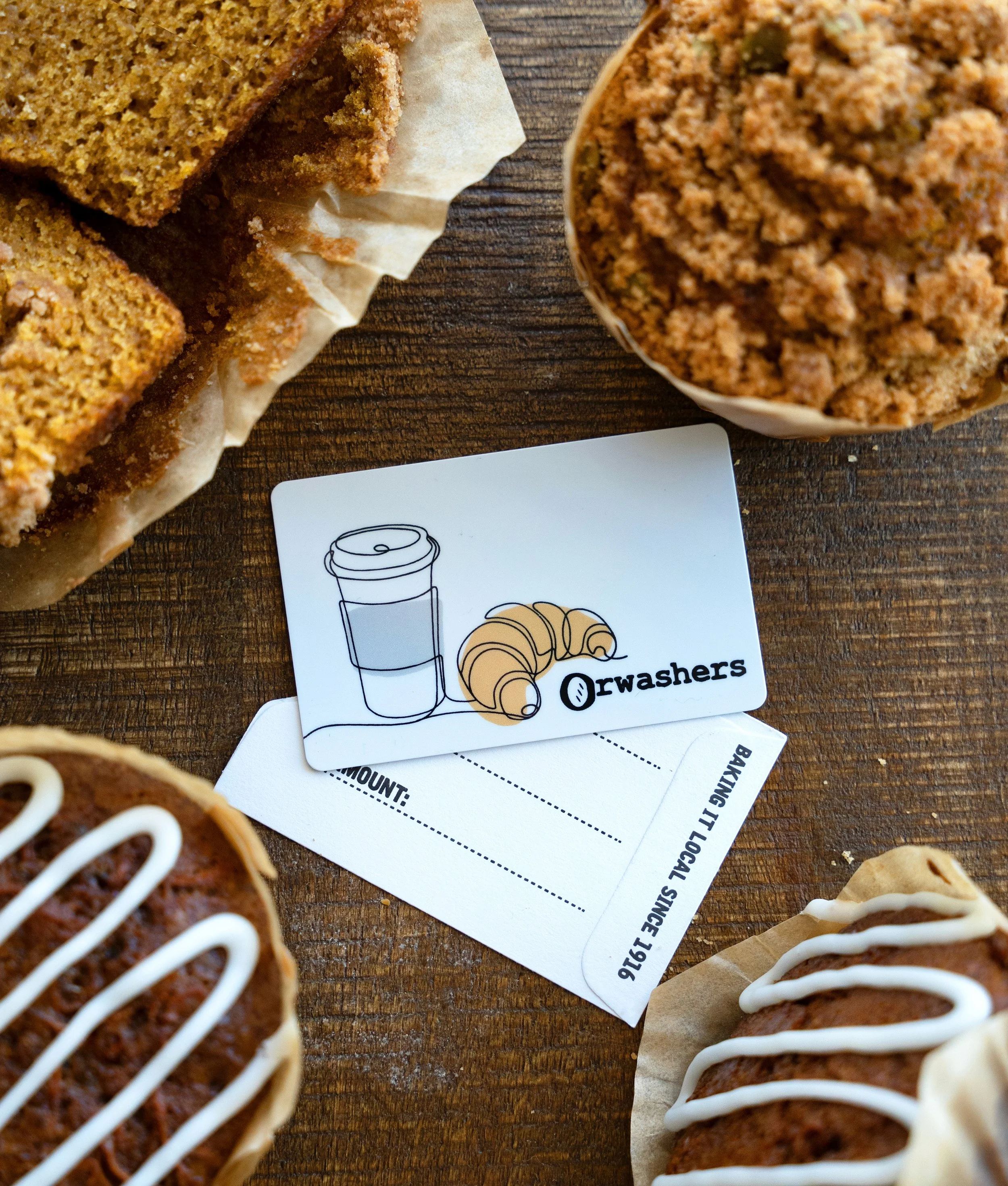 Orwashers gift card on a wood surface, surrounded by bakery treats.