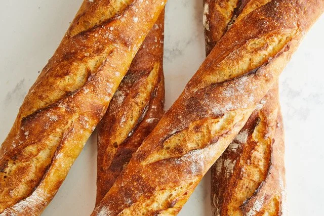 Four loaves of crusty baguettes arranged on a white surface.