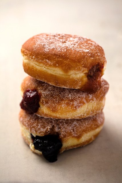 Stack of three jelly donuts oozing with fruit preserves and dusted with sugar crystals.