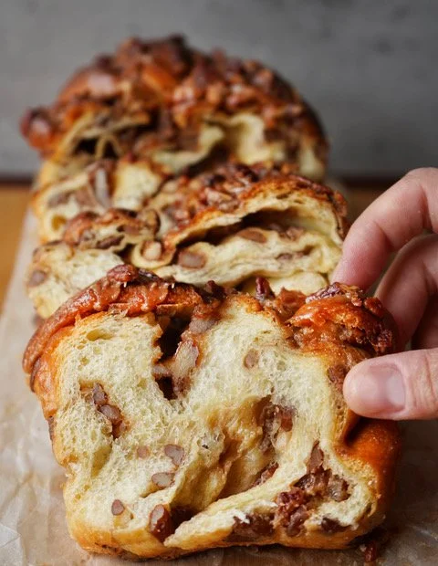 Fingertrips reaching for babka slices with airy soft interior and pecans swirled in and on top of the loaf.