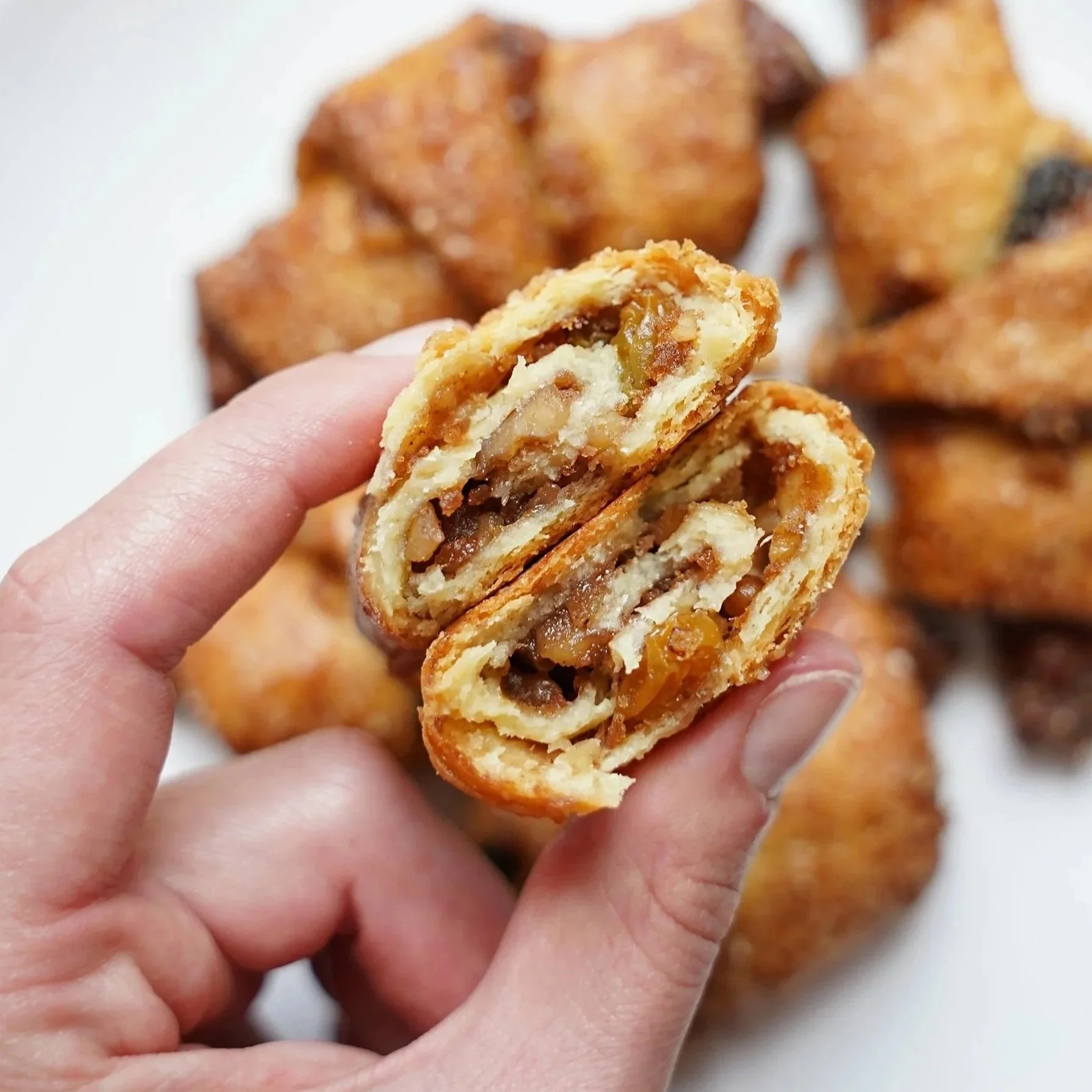 A rugelach cookie in a person's fingertips with rugelach in the background