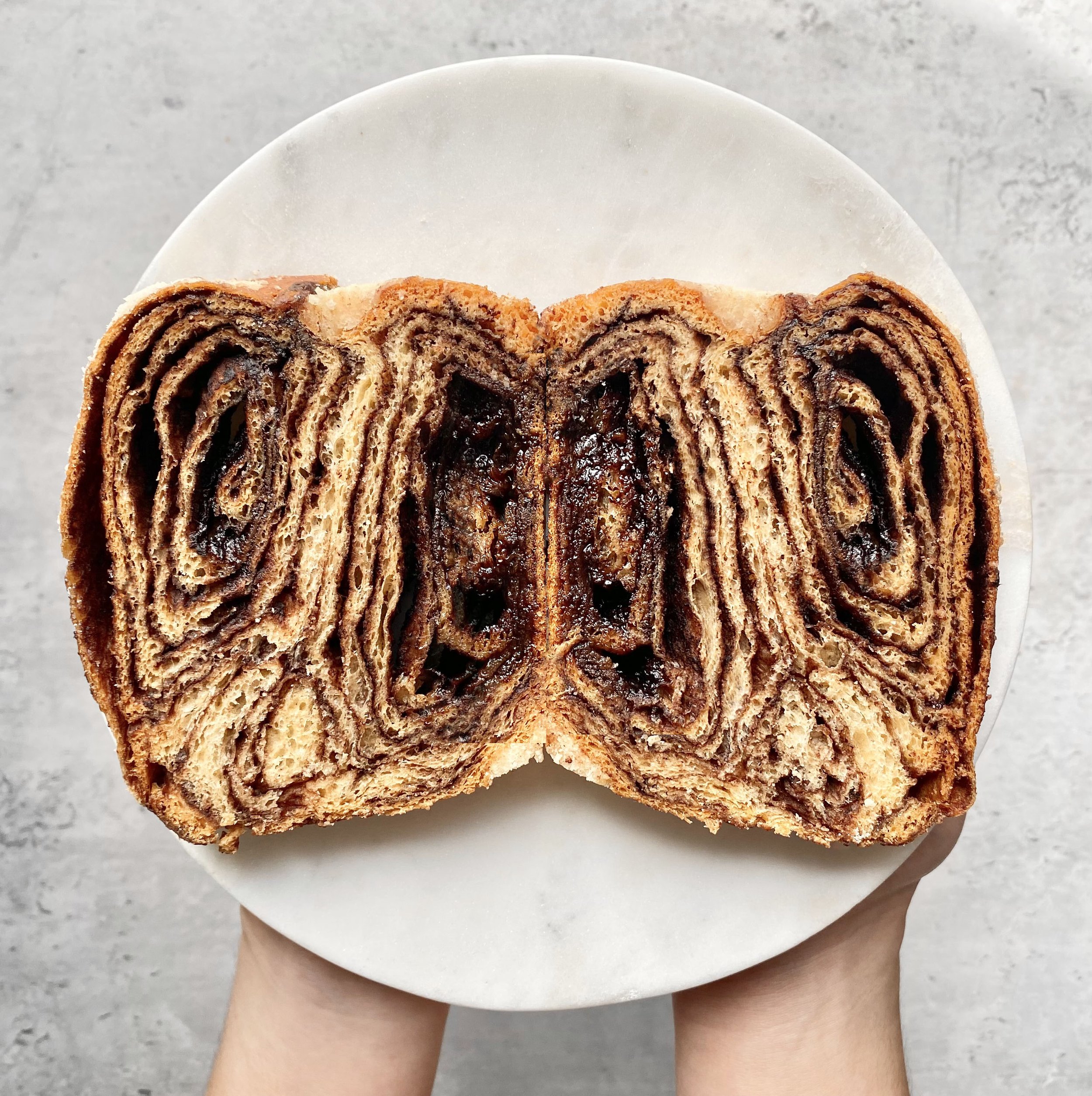 Fingertrips reaching for  babka slices with airy soft interior and pecans swirled in and on top of the loaf. 