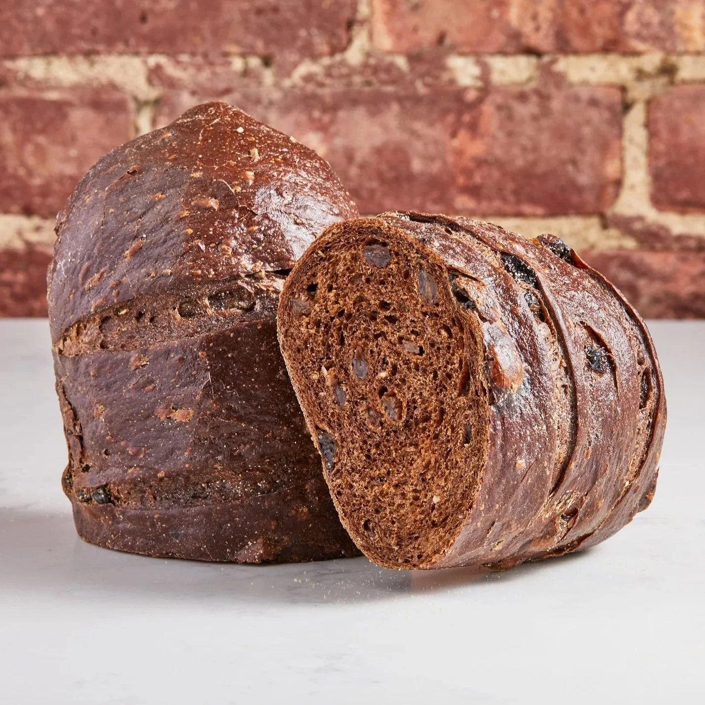 Loaf of traditional style dark pumpernickel bread against a brick background. 