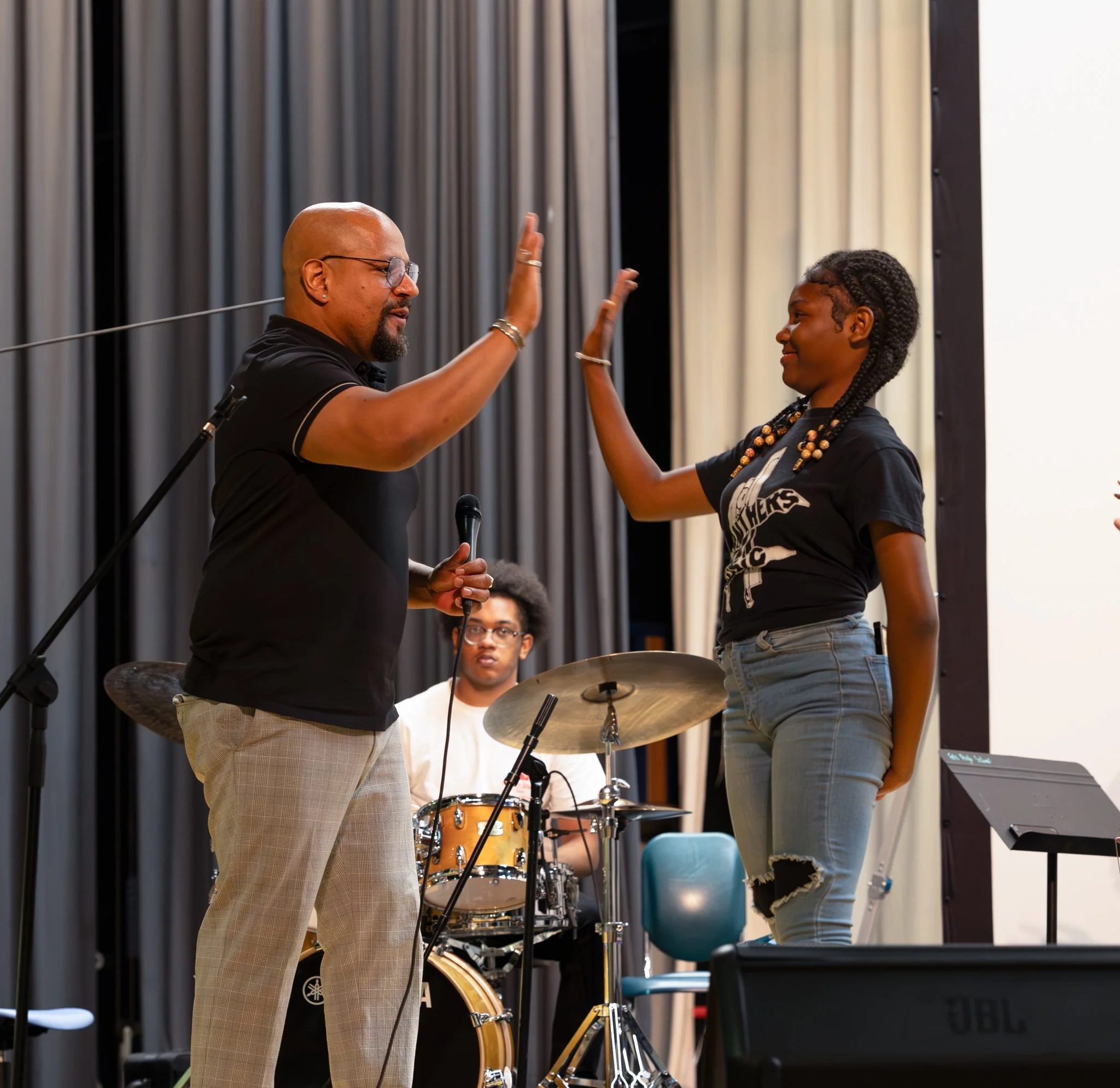 Three men playing jazz music outside using a saxophone, trumpet, and drum kit.