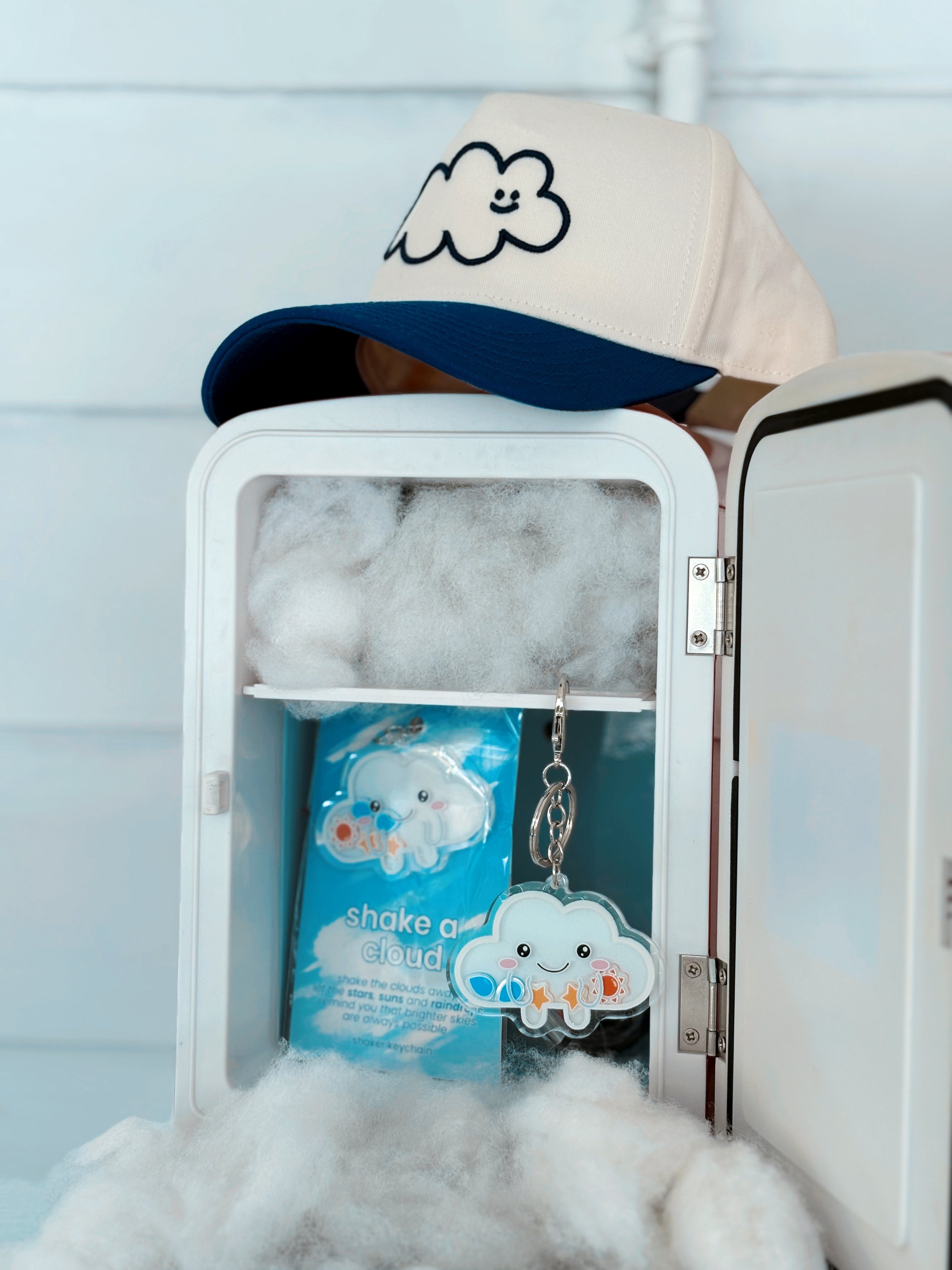 Cloud shaker keychains displayed inside a pastel mini fridge with The Head in the Clouds Hat resting on top.