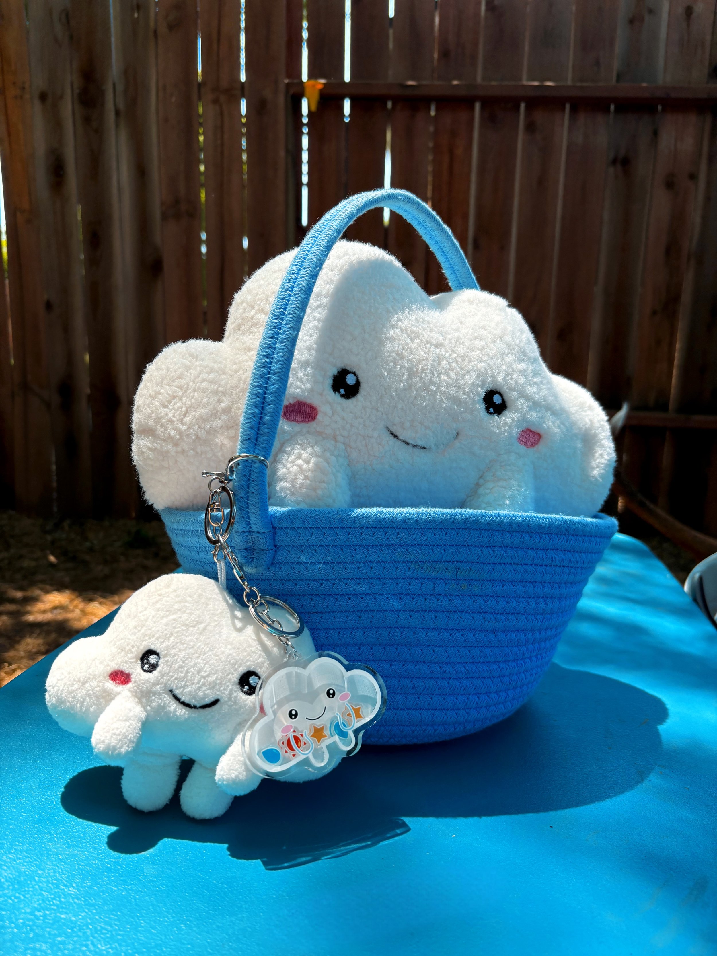 Cloud shaker keychain attached to the handle of a blue basket holding the Carry a Cloud Plush Charm and a Cuddle a Cloud Plush, styled together for a soft and cozy display