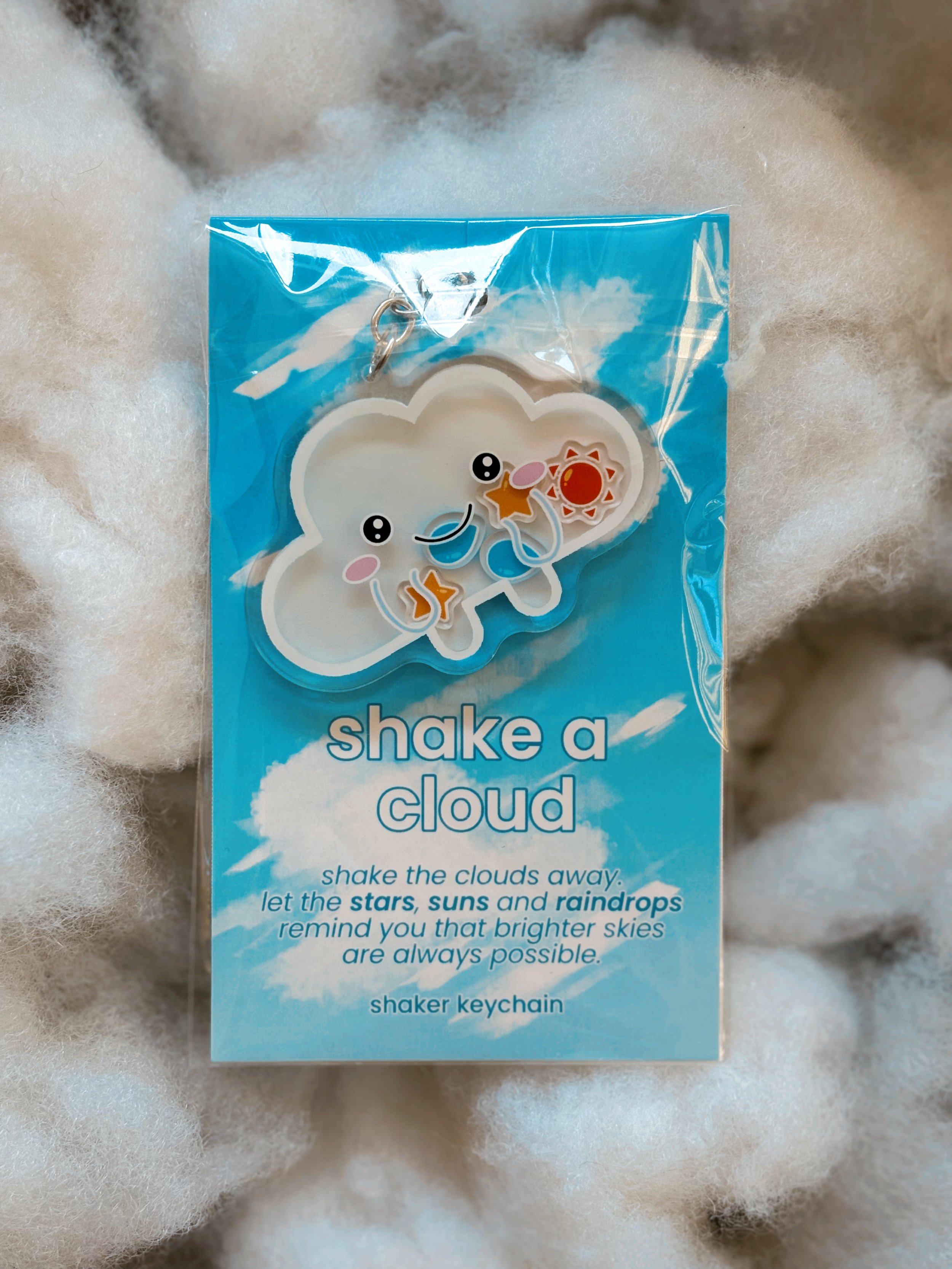 Cloud shaker keychain displayed on a backing card placed on soft stuffing styled to look like clouds