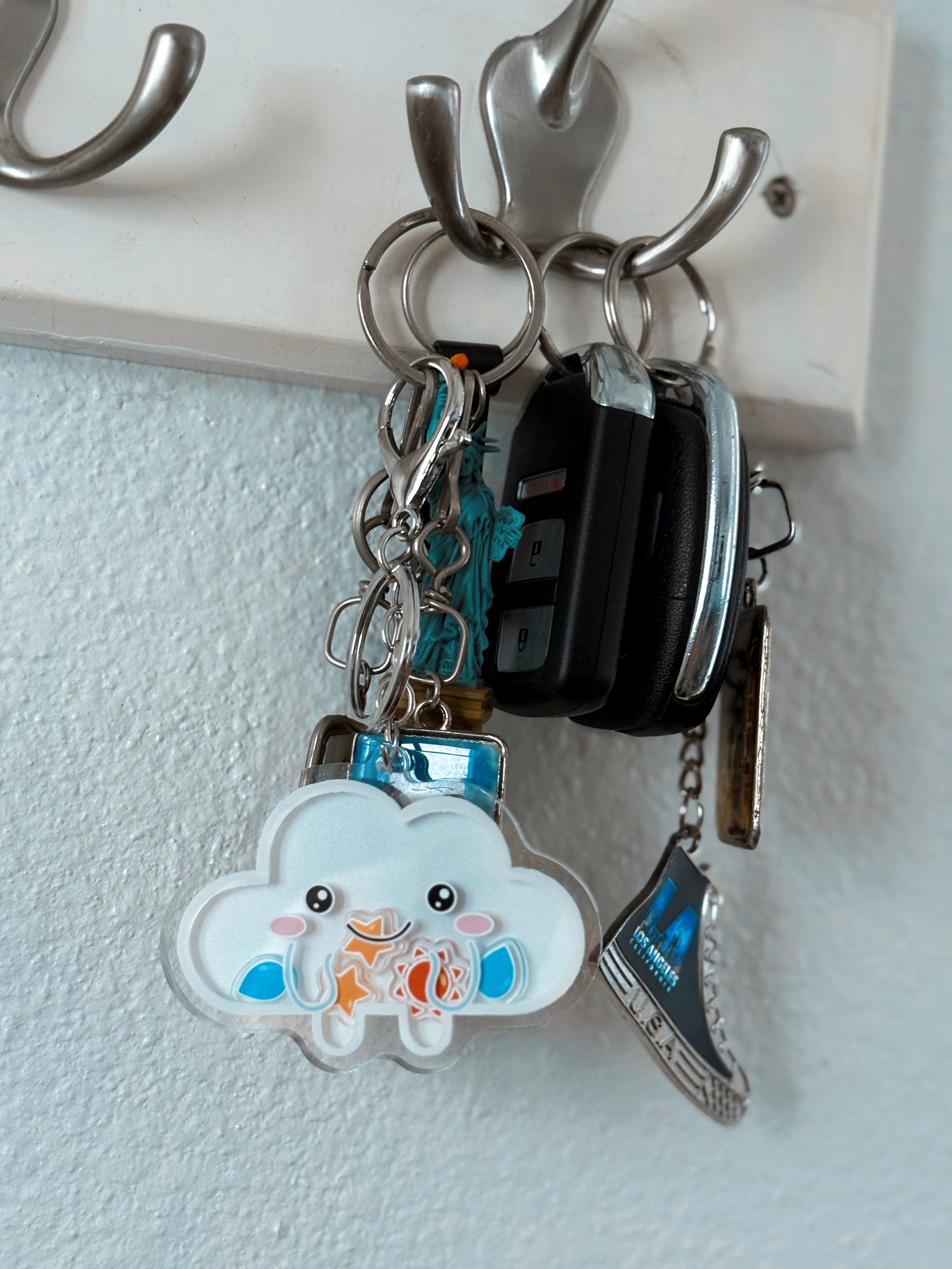 Cloud shaker keychain hanging on a set of keys from wall-mounted key hooks, showcasing a cute and functional accessory in an everyday home setting.