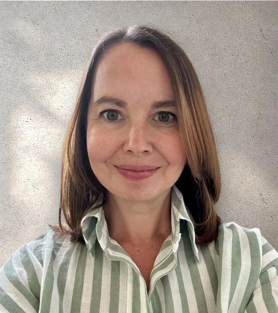 Portrait of a woman with shoulder-length brown hair, wearing a white and green striped shirt, smiling against a gray background.