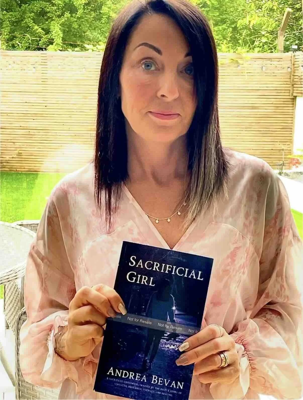 Author holding her book Sacrificial girl in a garden on a summers day.jpeg