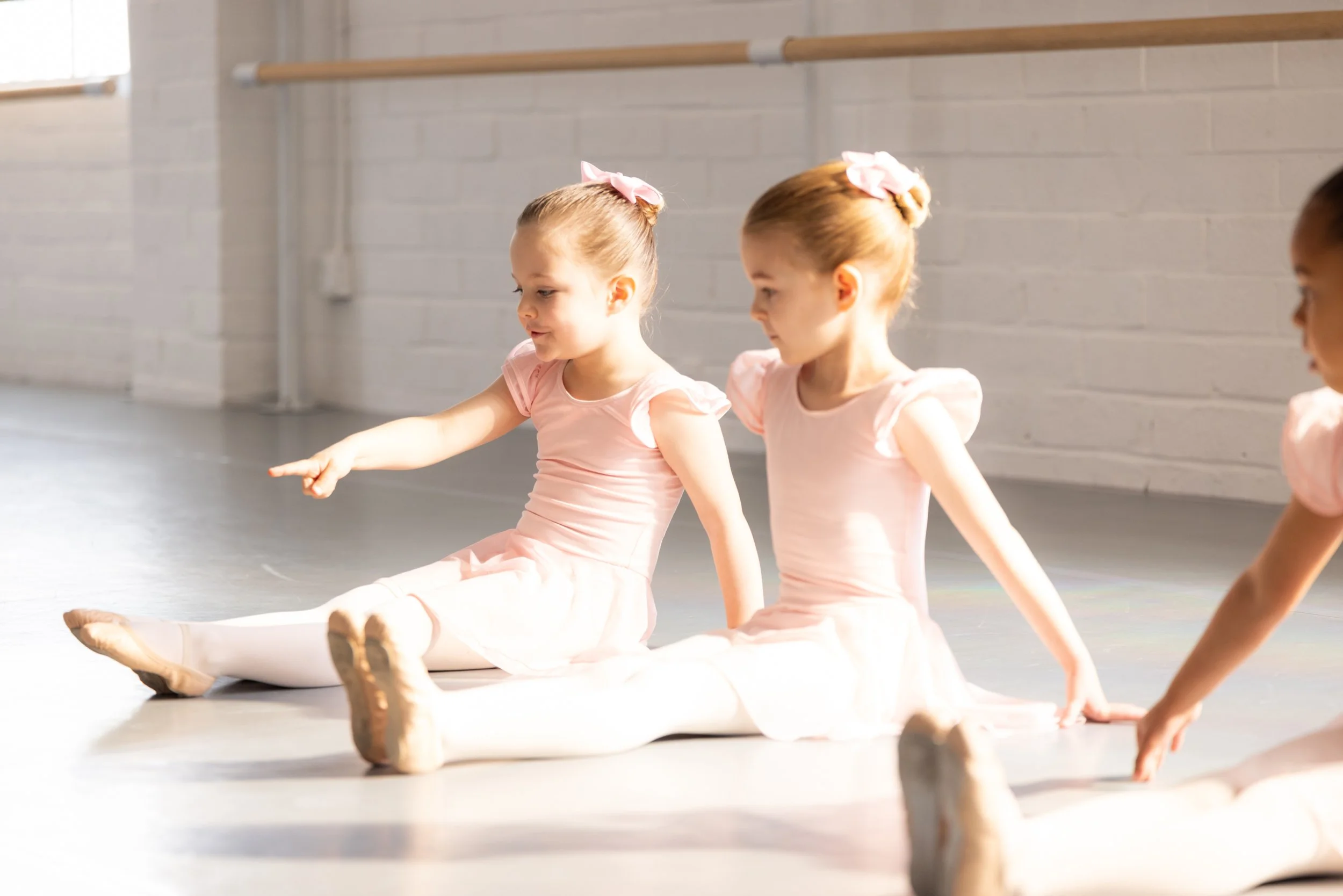 Young ballet dancers sitting on the floor and smiling in ballet class