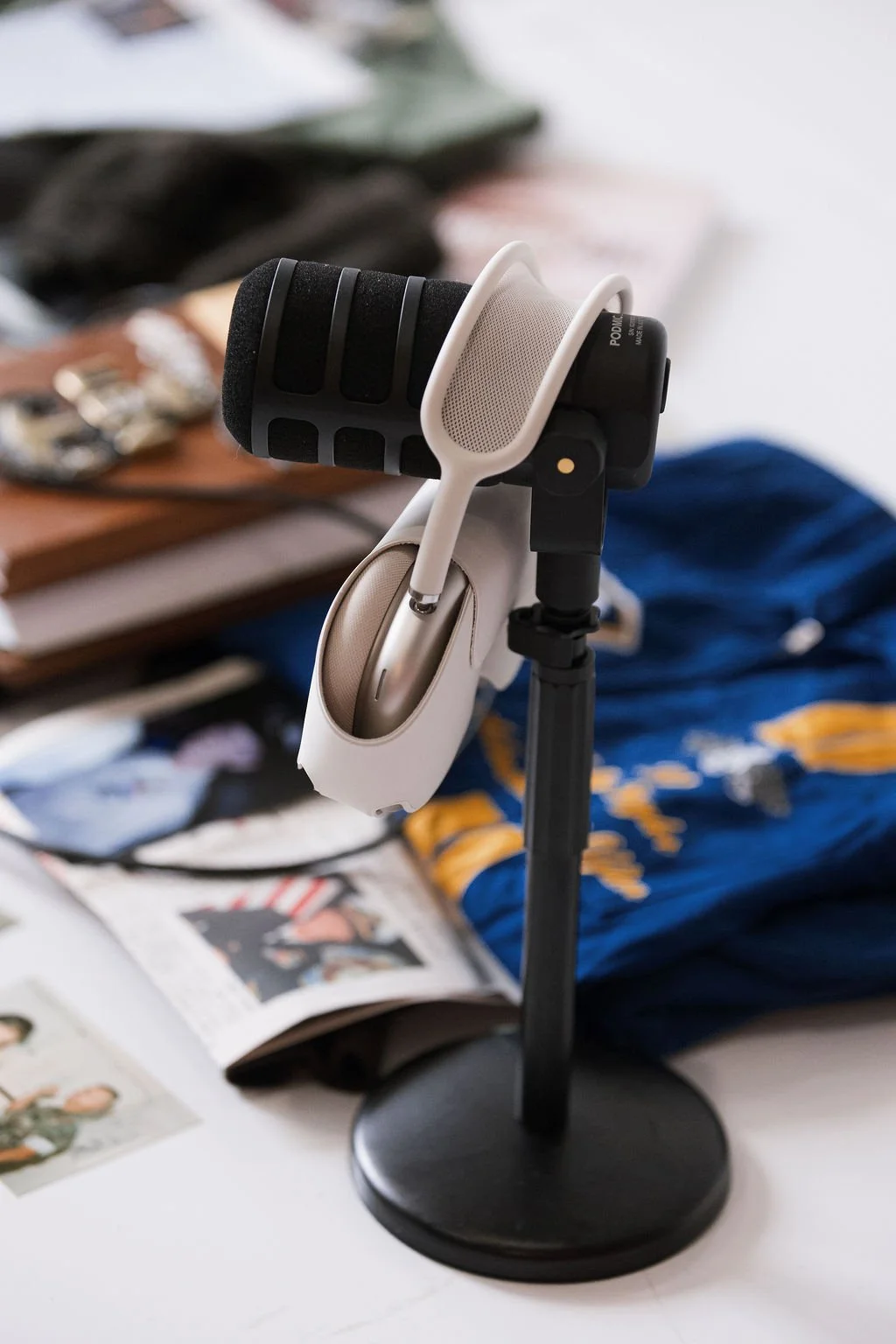 Microphone mounted on a stand in front of a collage of military newspaper clippings, jackets, and more with a pair of headphones on top of the microphone.