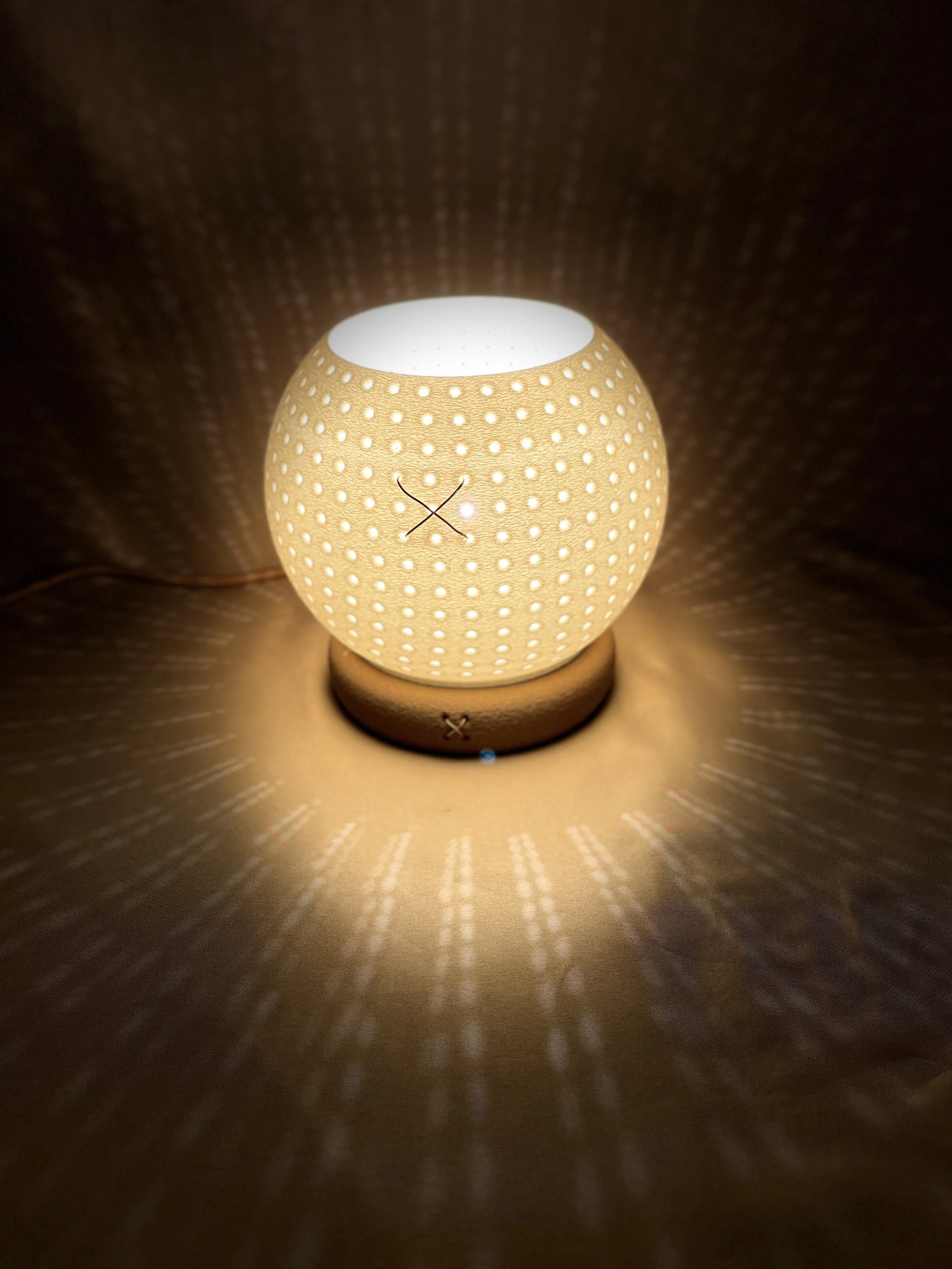 A decorative lamp with a spherical shape and a perforated surface, emitting warm light and casting intricate light patterns on the surrounding surface.