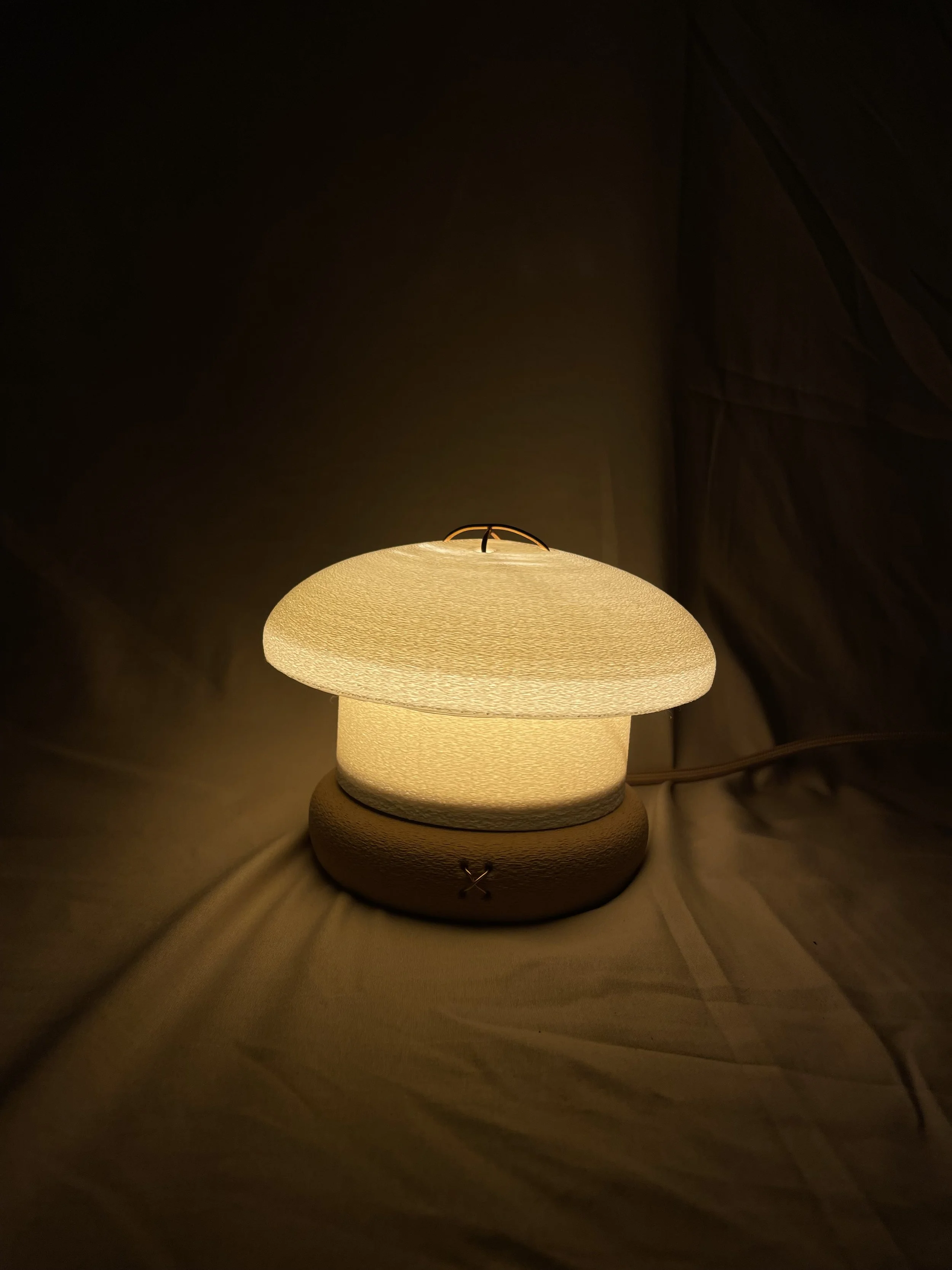 A table lamp with a textured, mushroom-shaped shade emitting a warm, soft glow in a dark room.