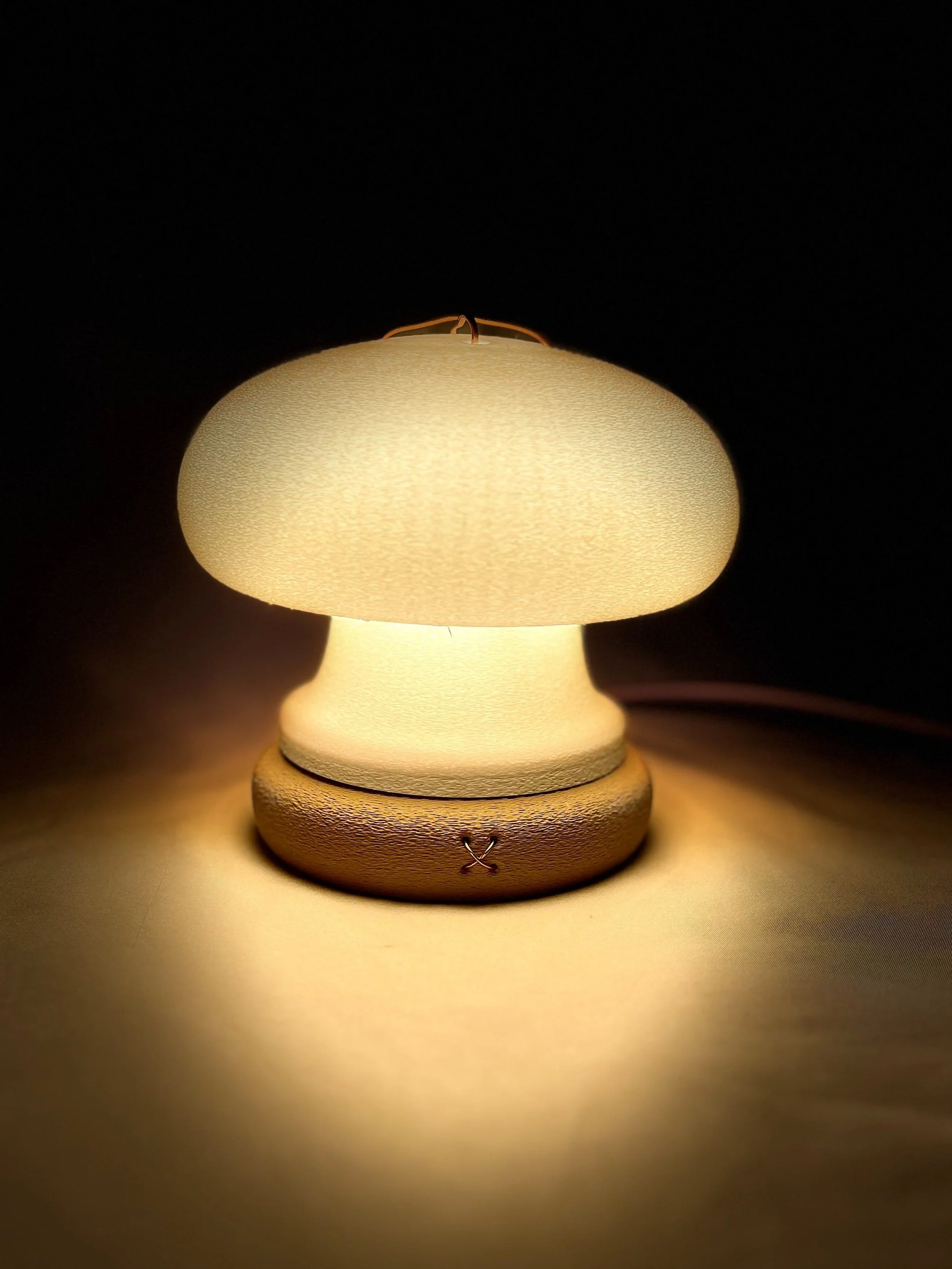 Small table lamp with a beige lampshade emitting warm light against a dark background.