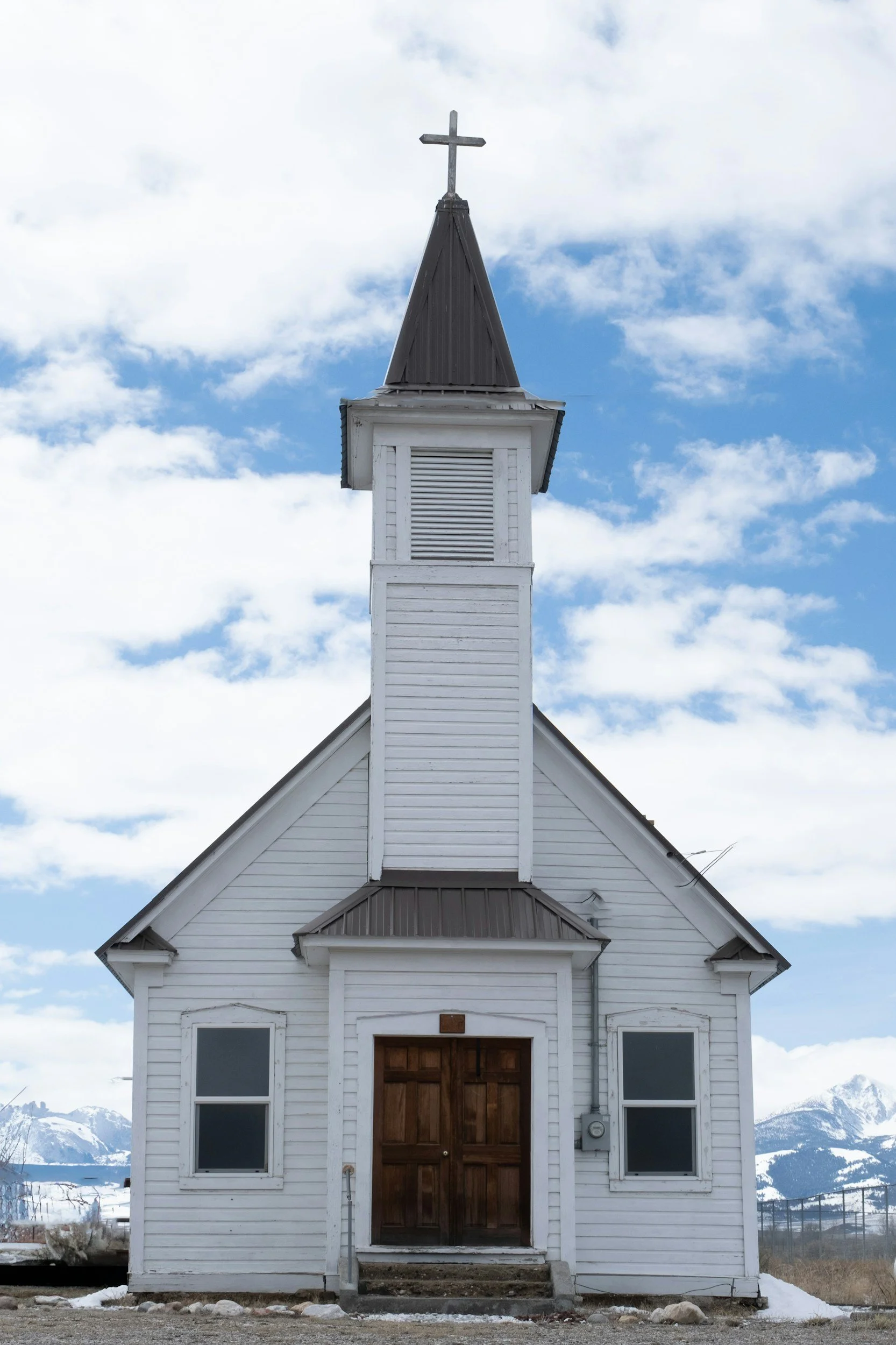 front view of a small, older white church with two windows and a steeple.