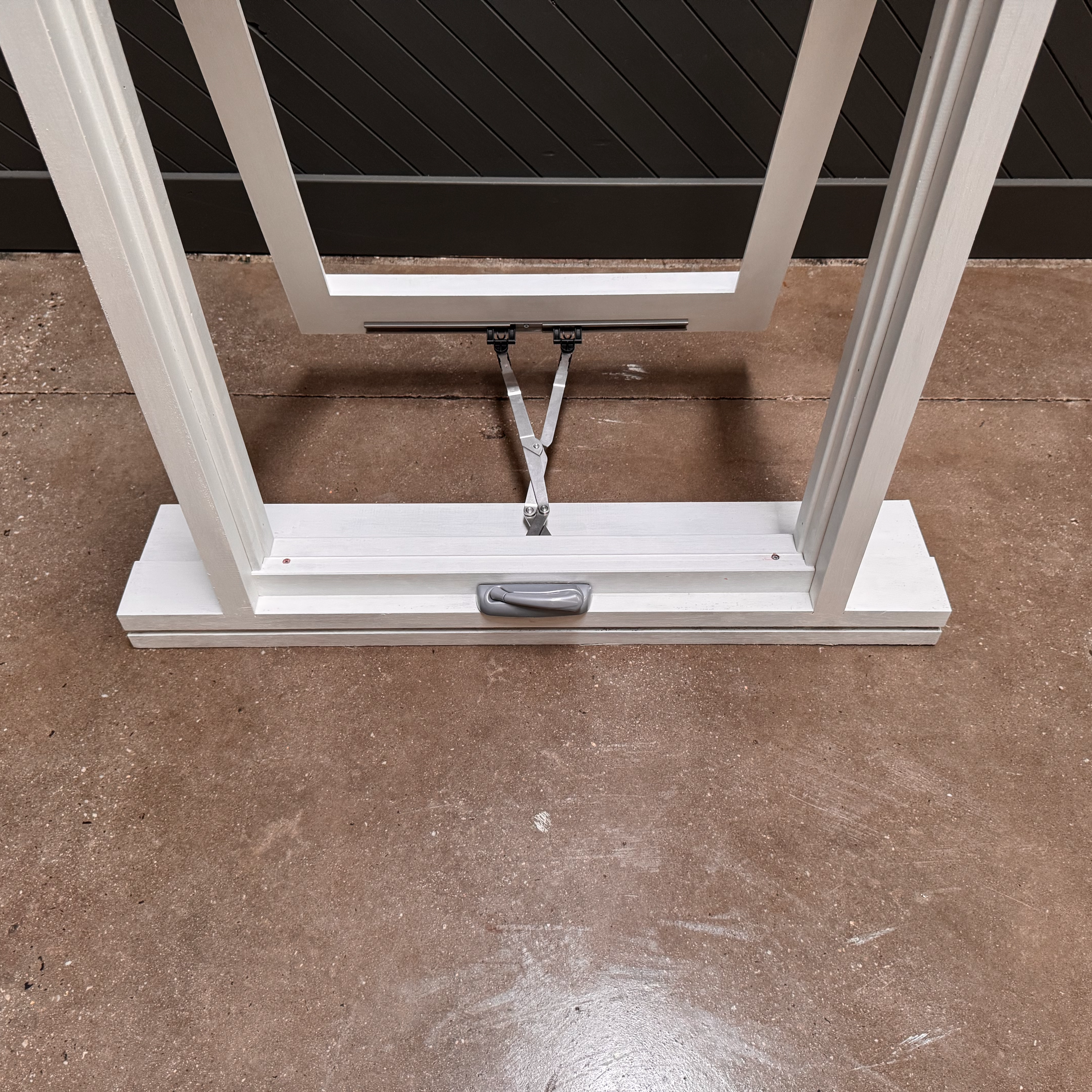 A metal and white wooden frame structure with a small handle at the bottom, situated on a concrete floor, with a black and white striped fence in the background.