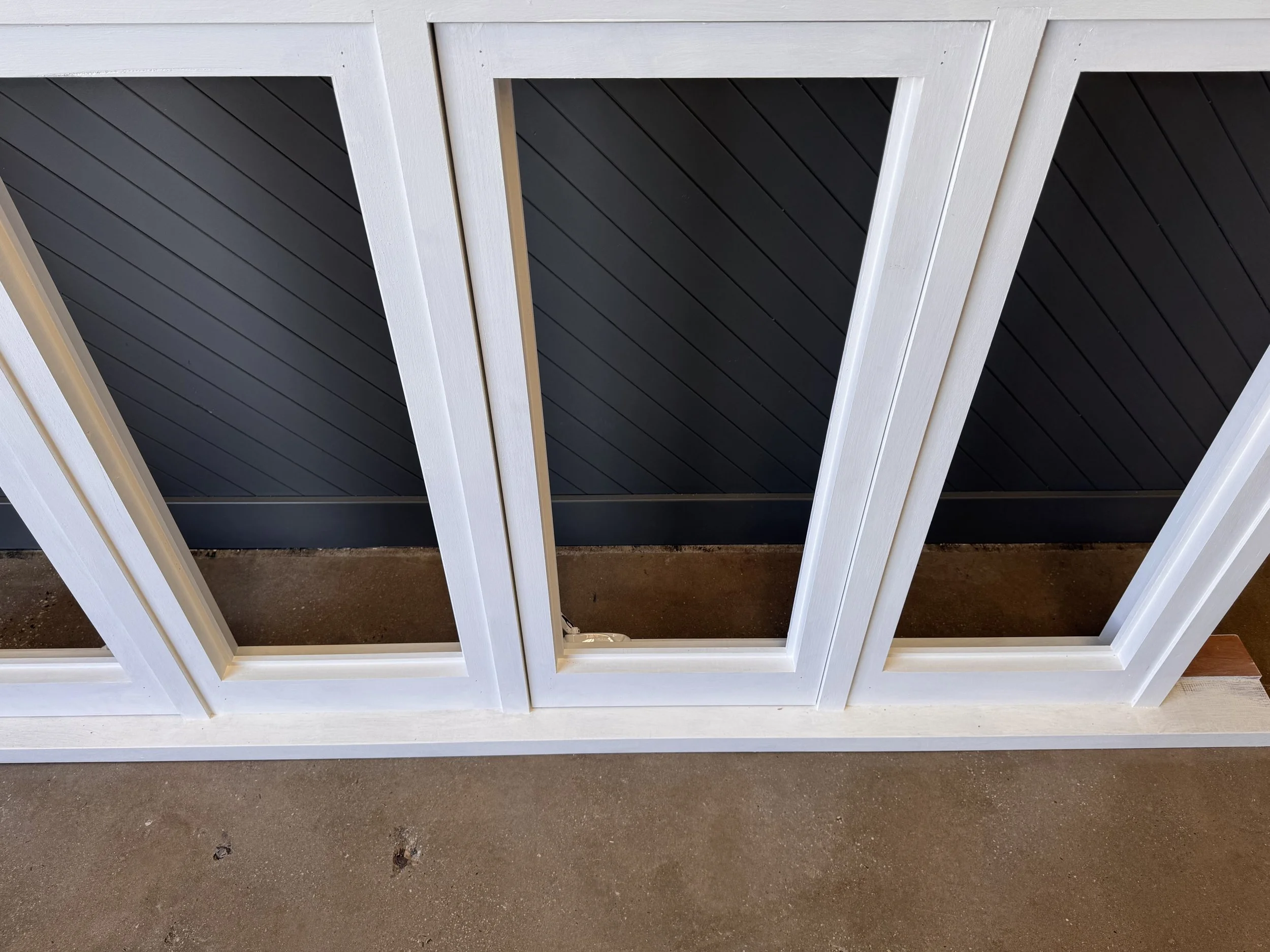 Close-up of a black and white framed window or door with black slatted background, placed on a brown concrete surface.