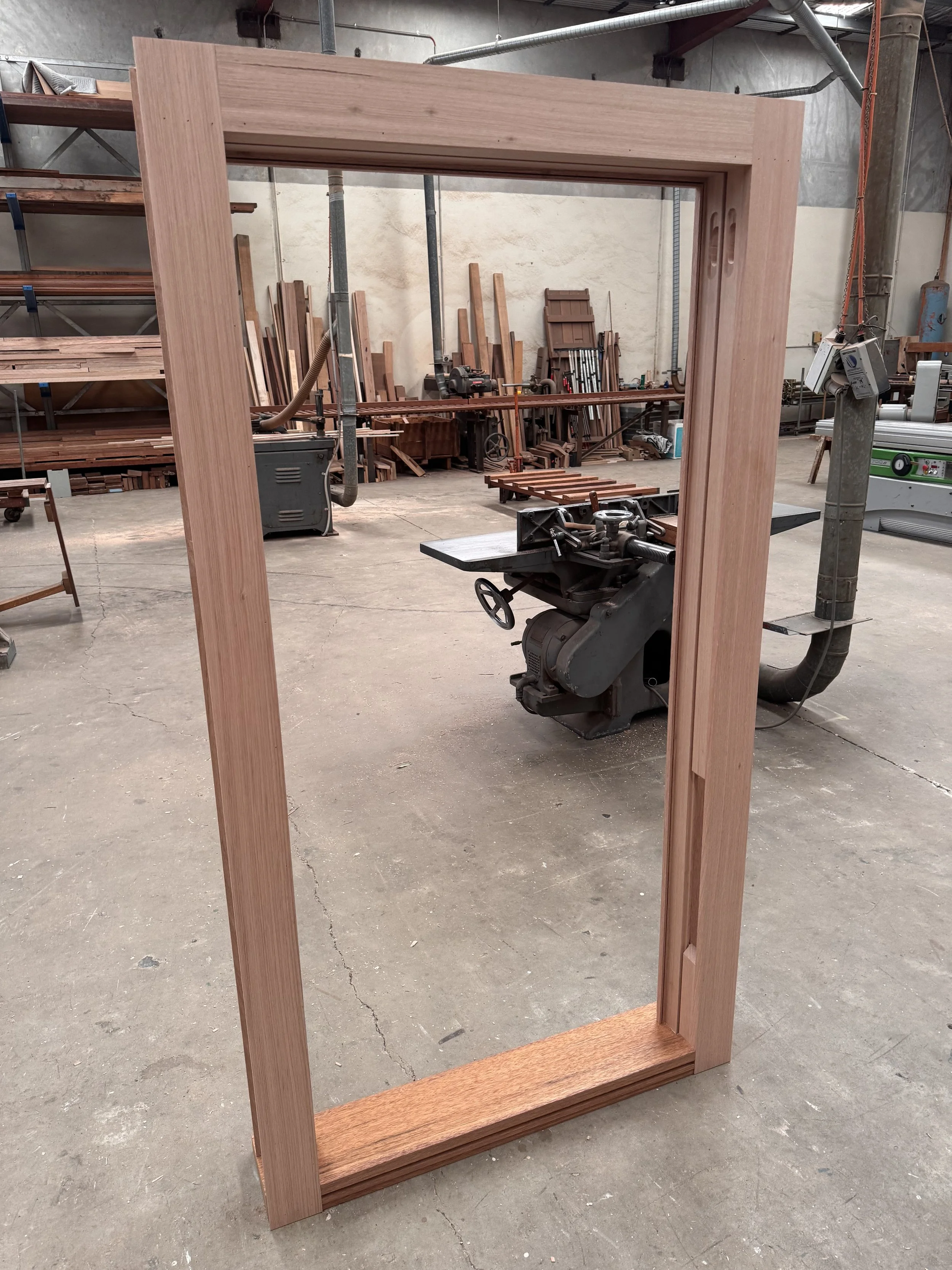 A wooden picture frame standing upright in a woodworking shop.