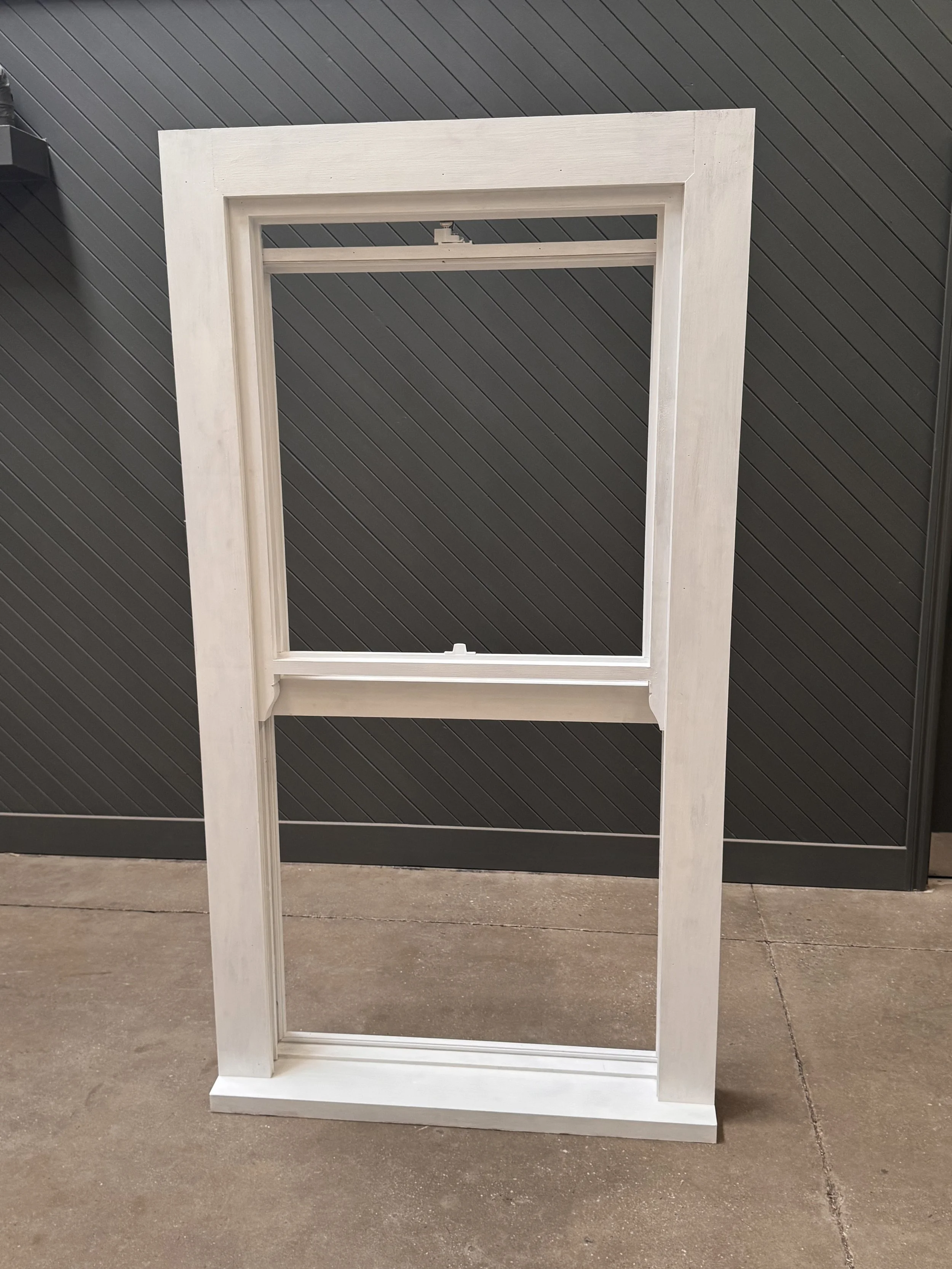 Unassembled white window frame standing on concrete surface against a dark wall.