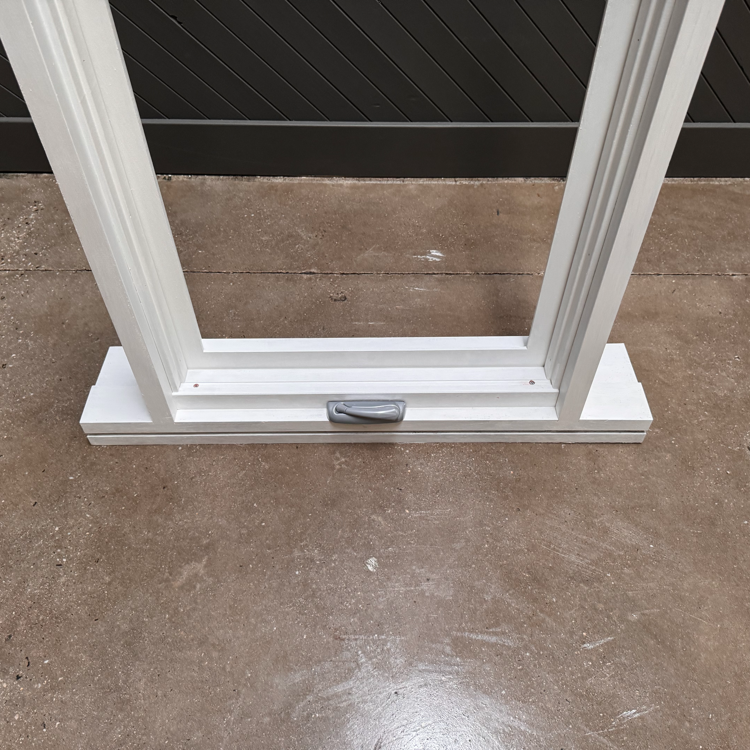 Empty white metal window frame with a handle, placed on a concrete floor outside.