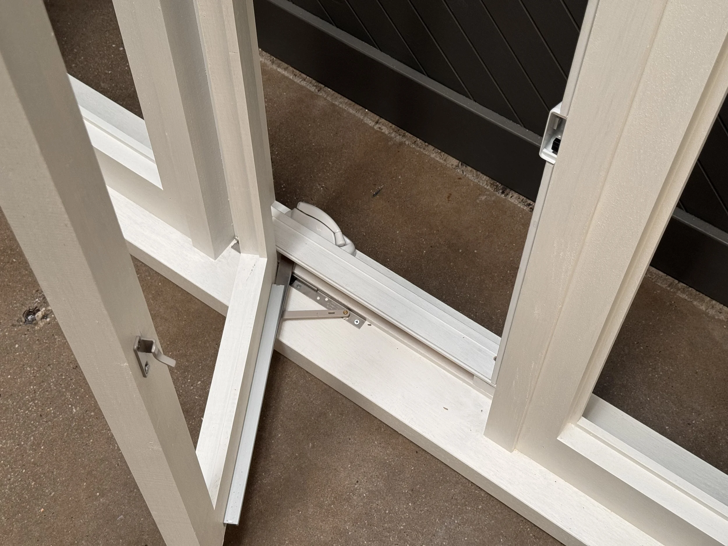 Close-up view of a white adjustable door hinge mechanism on a white door frame, with a black background and brown floor surface.