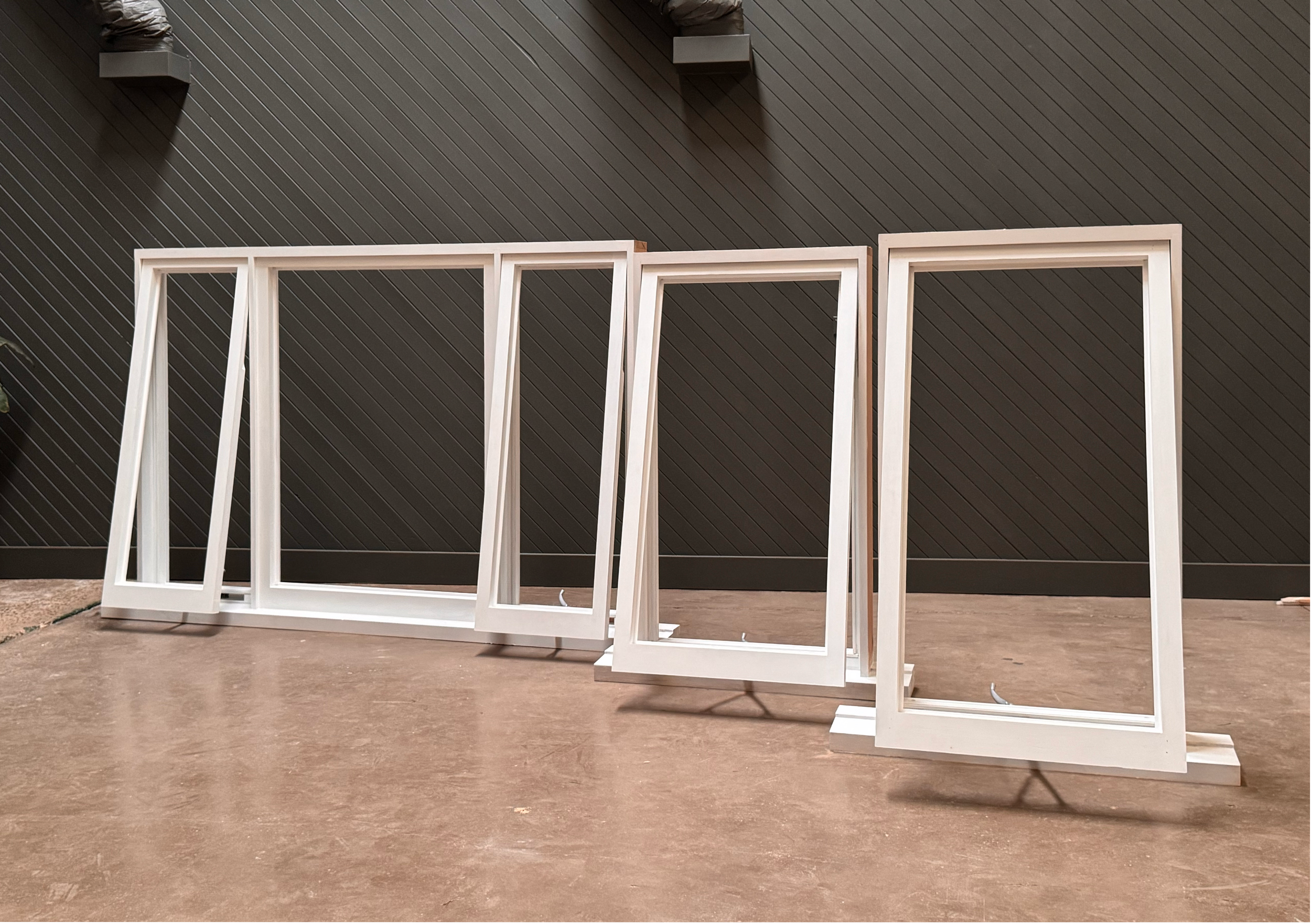Four white window frames leaning against a dark wall, with some potted plants and packaging visible on the wall.