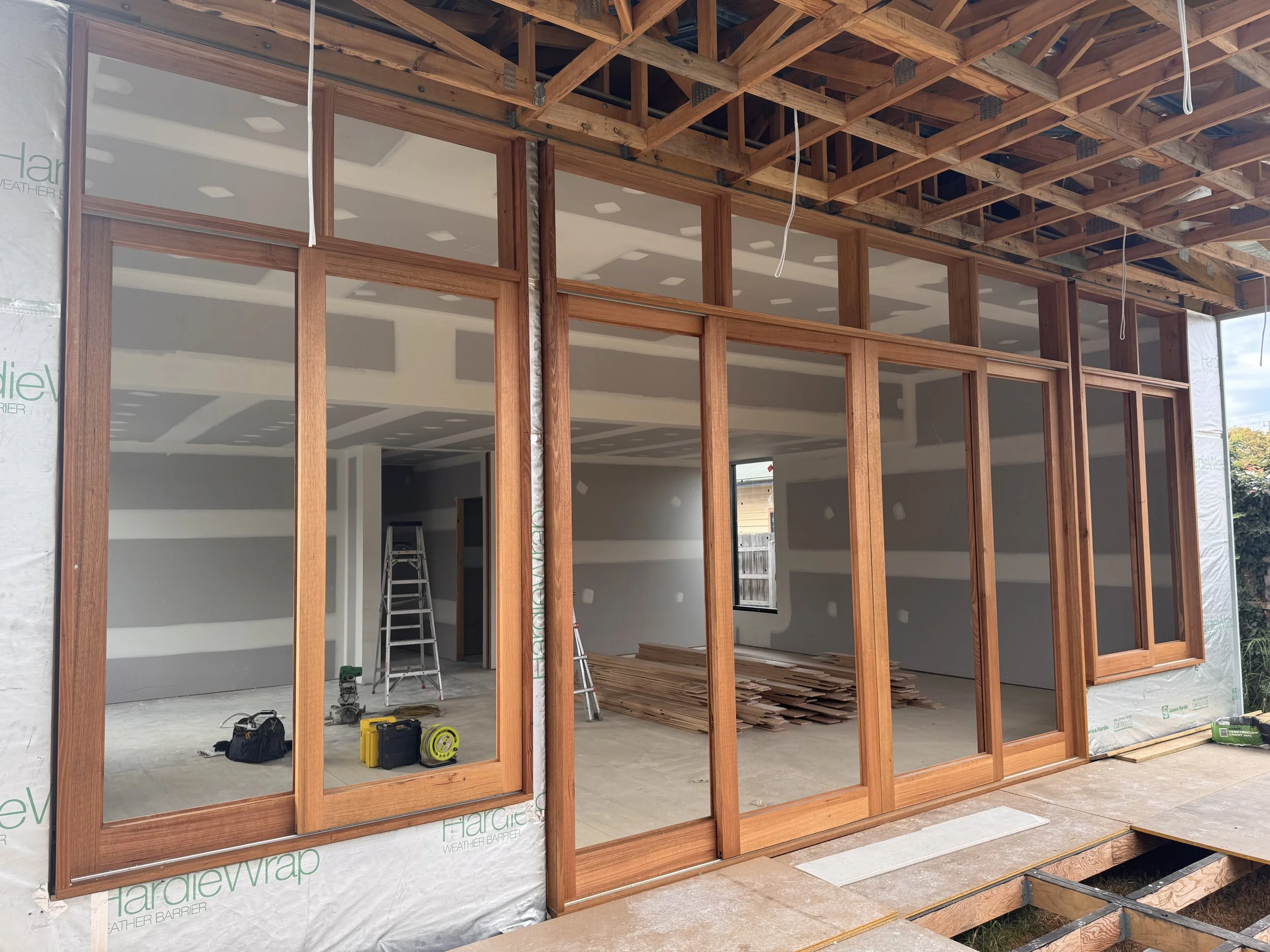 Construction site of a house with wooden framing and partial drywall, windows installed, construction tools on the floor.