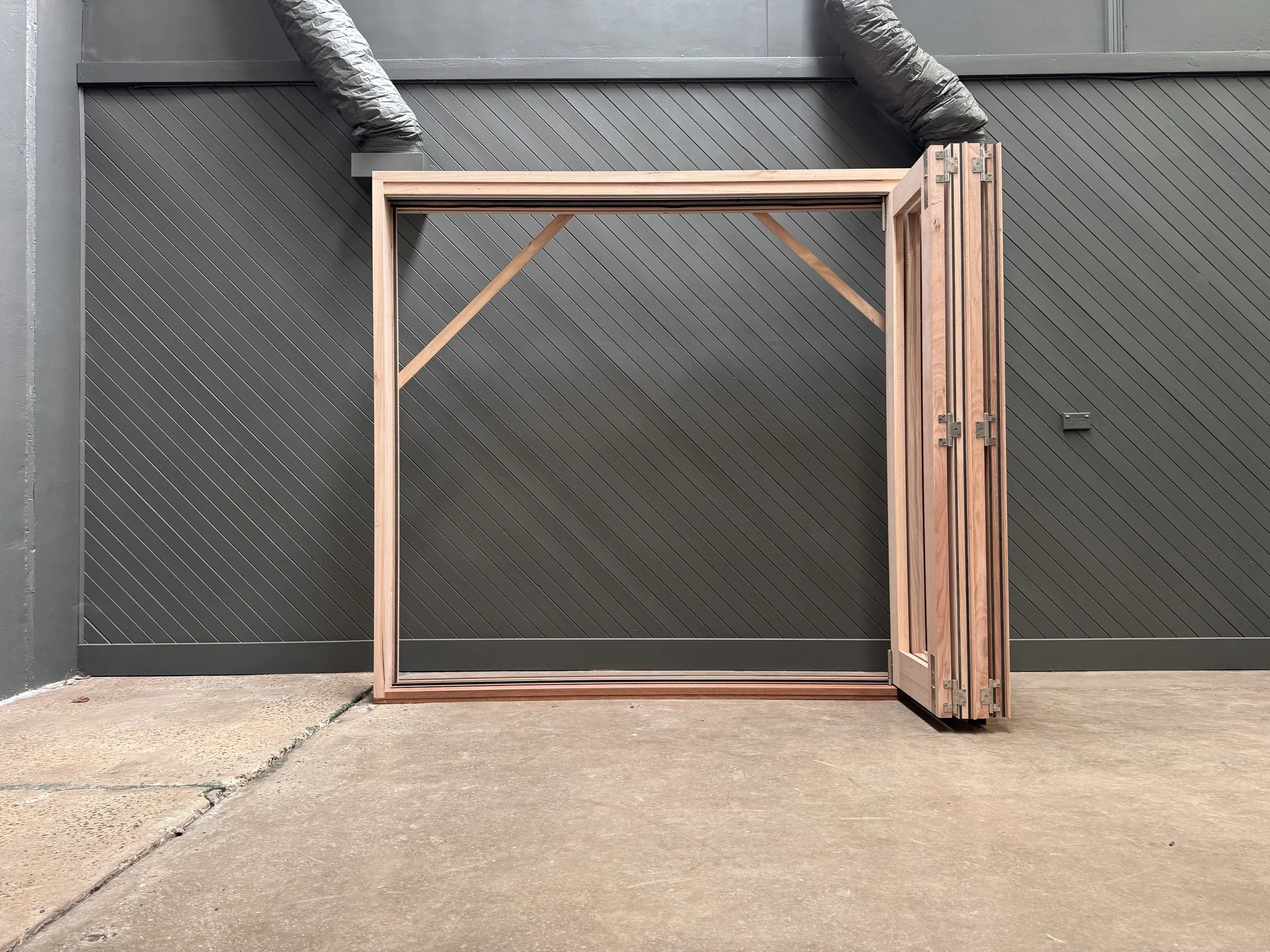 Unassembled wooden door frame and door leaning against a dark gray metal wall outside on a concrete ground.