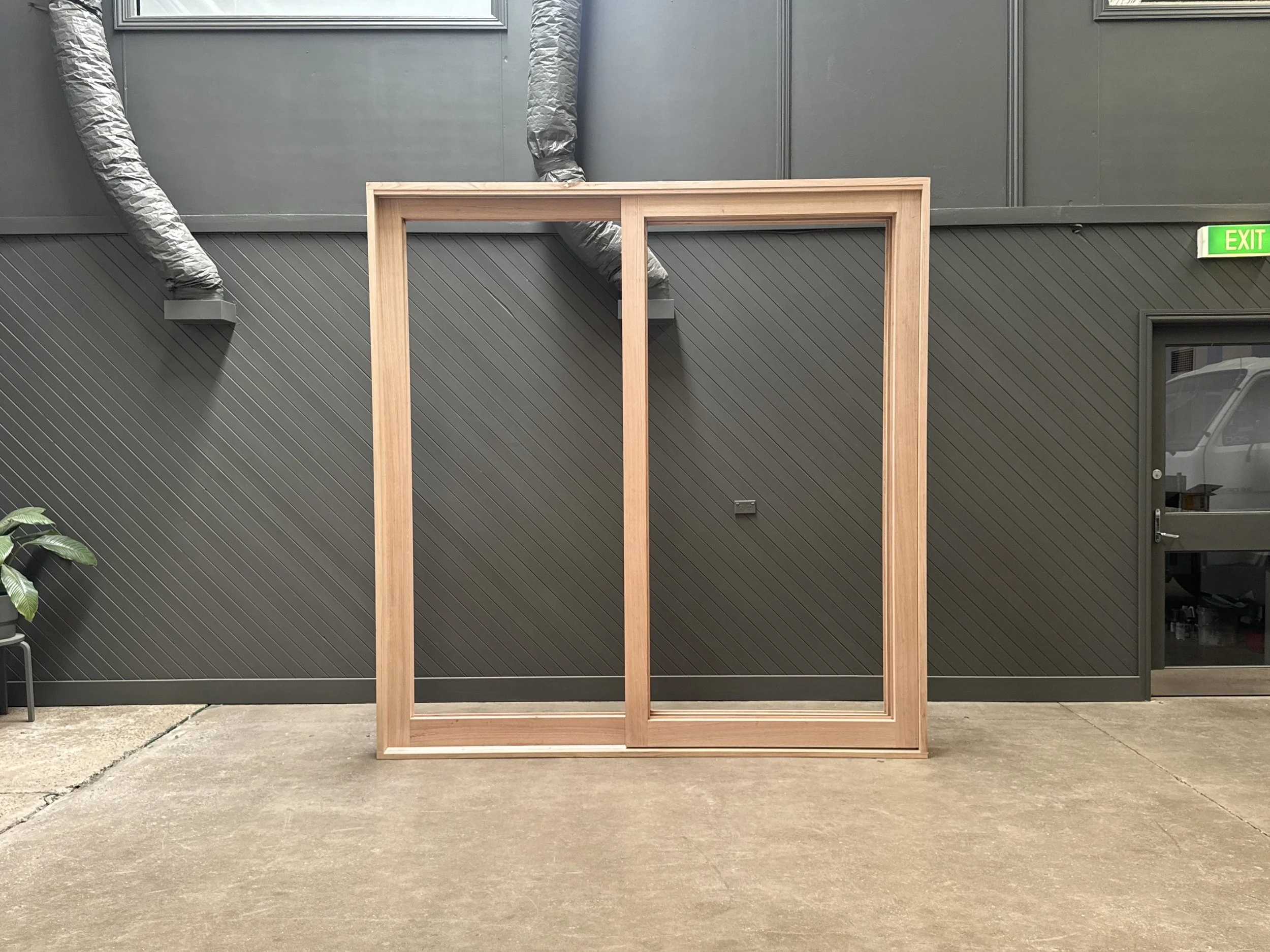 Empty wooden picture frame standing on concrete floor against a gray wall with ductwork in an industrial space.