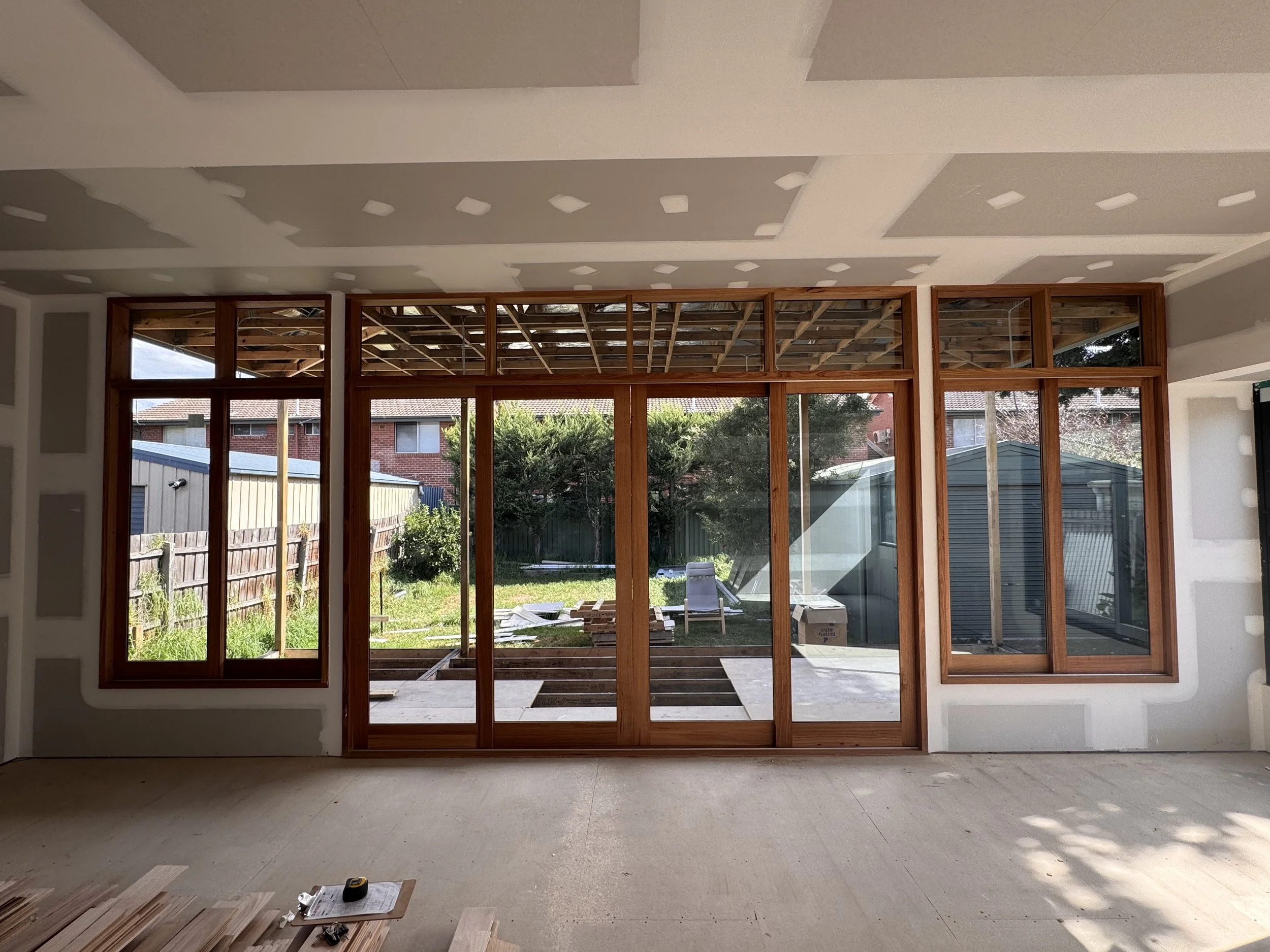 Interior view of a room under construction with large glass window framing and an unfinished outdoor deck area.