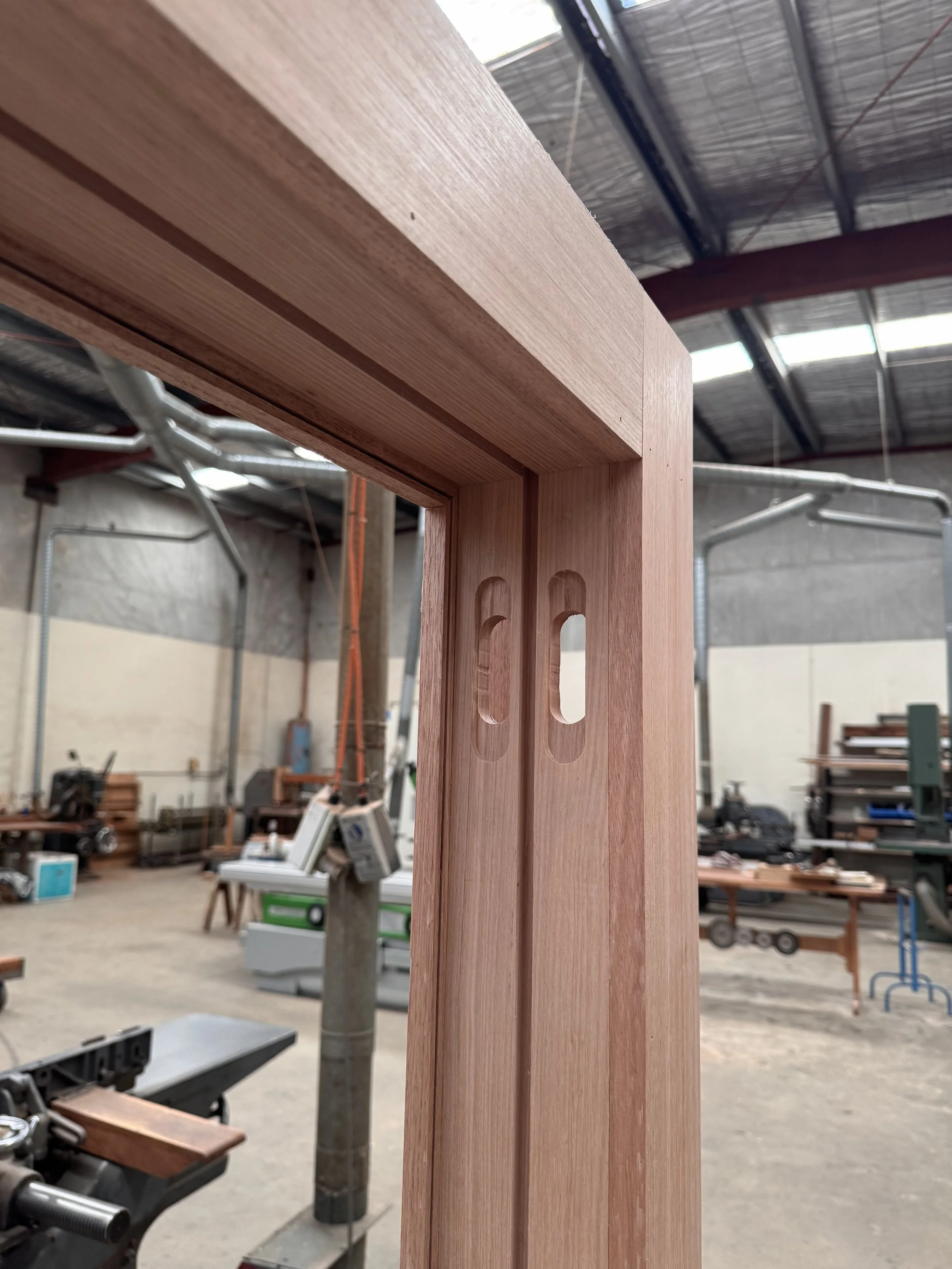 Close-up of a wooden frame with multiple oval cutouts in a workshop.