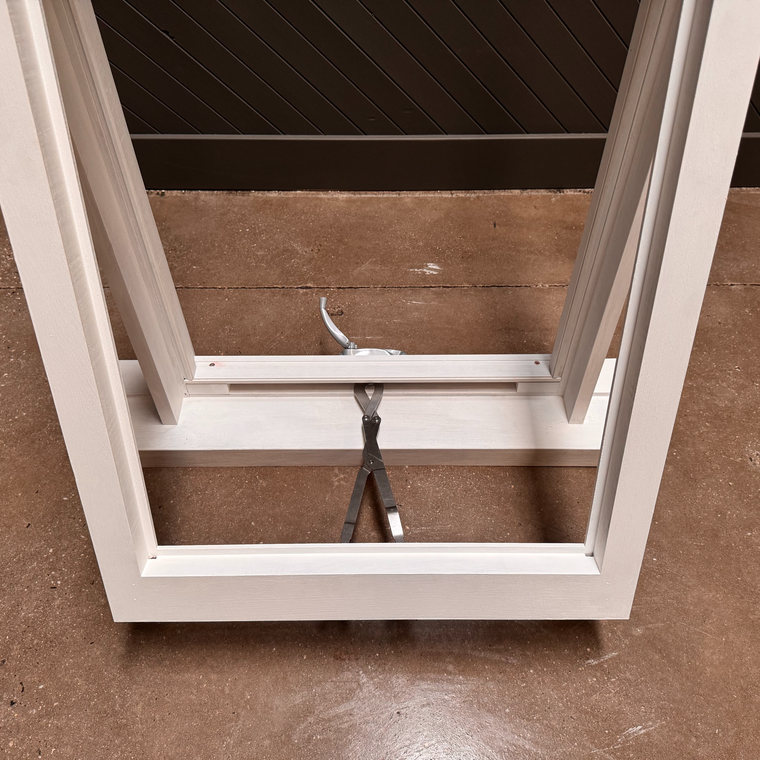 View of an unfinished wooden cabinet frame with a metal clamp inside, on a brown concrete floor.