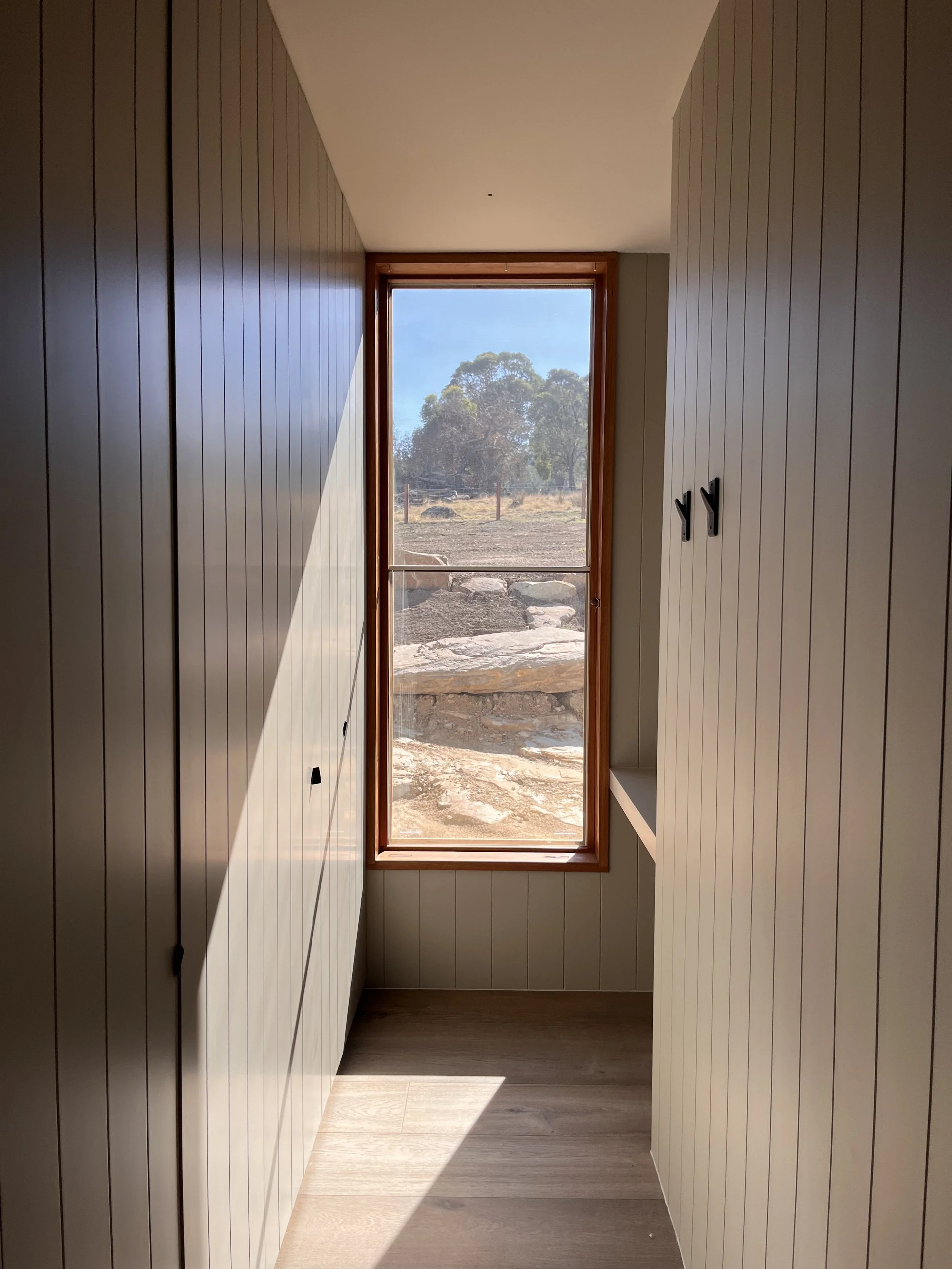 Interior of a narrow room with wood-paneled walls and a window showing an outdoor landscape with rocks and trees.