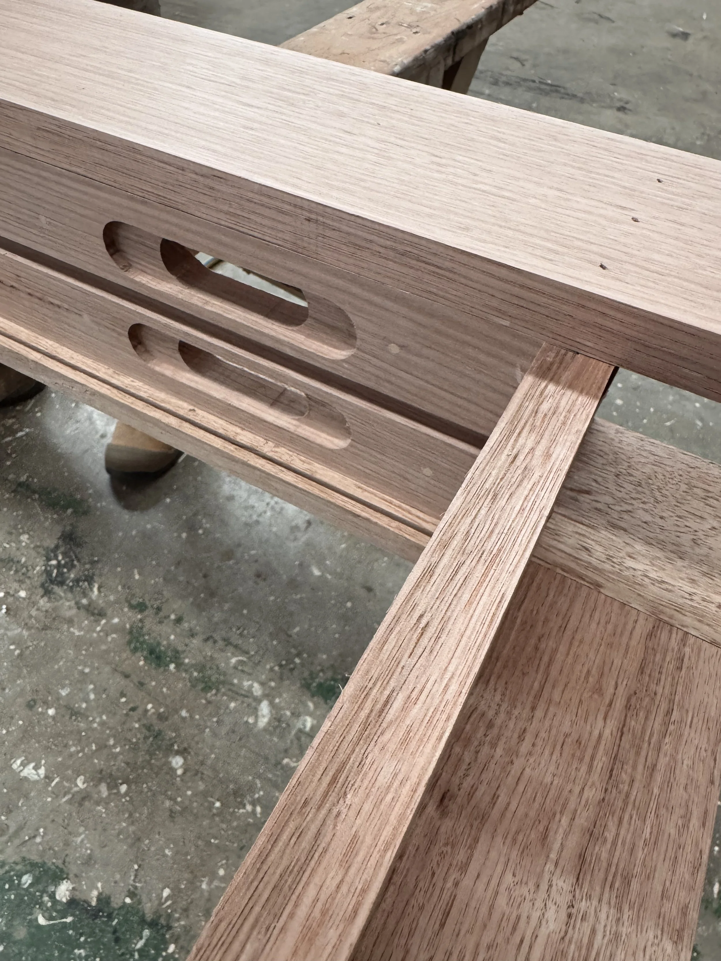 Close-up of unfinished wooden furniture with two elongated oval cutouts and a wooden support.