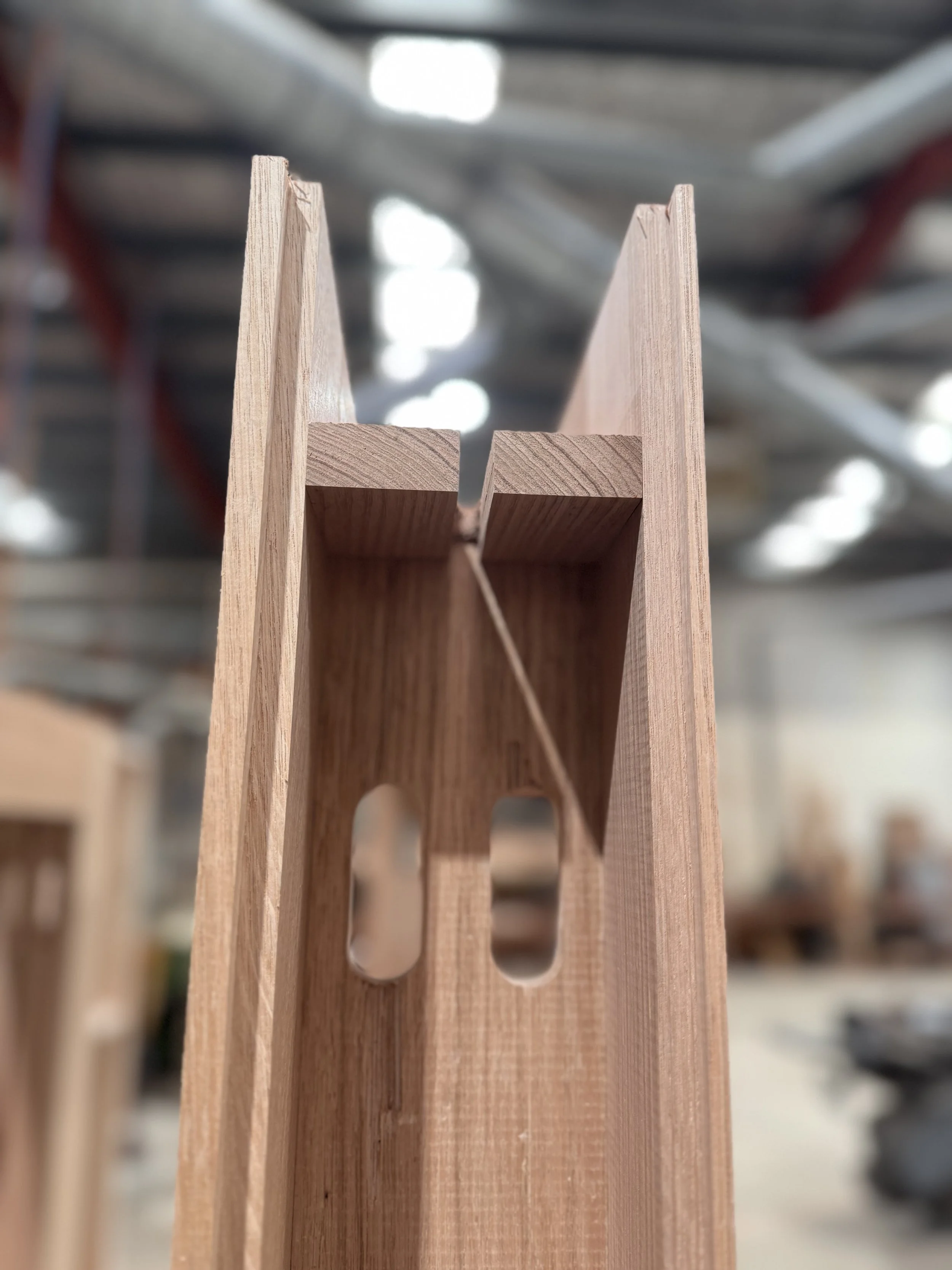 Close-up of a wooden chair frame with vertical and horizontal pieces, showing a notched joint, in a woodworking shop.
