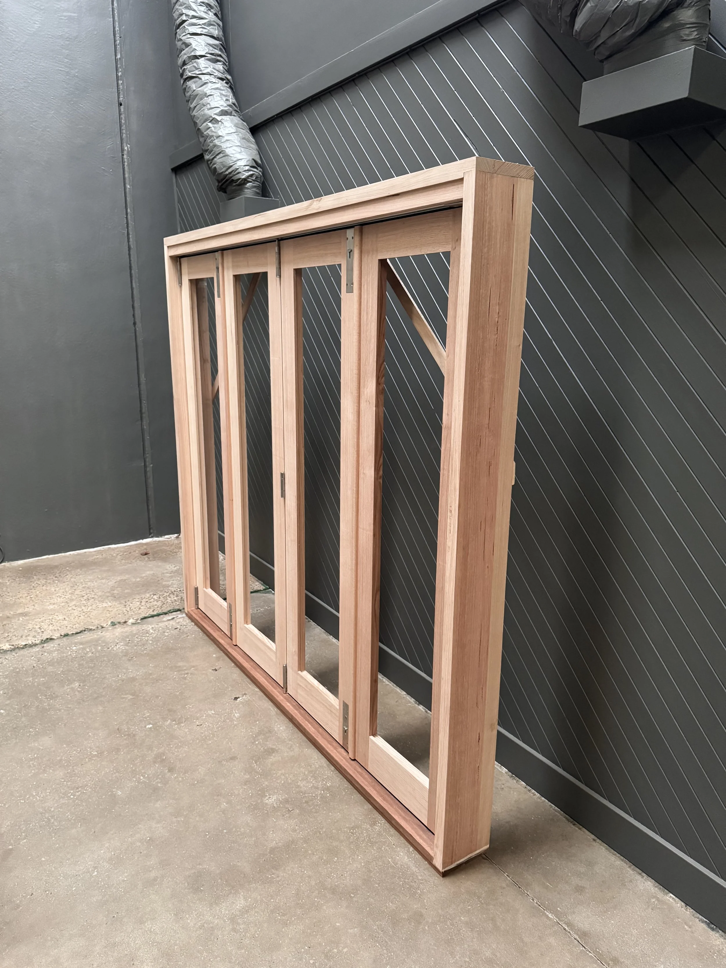 Unfinished wooden door or window frame leaning against a black wall inside a room with concrete flooring.