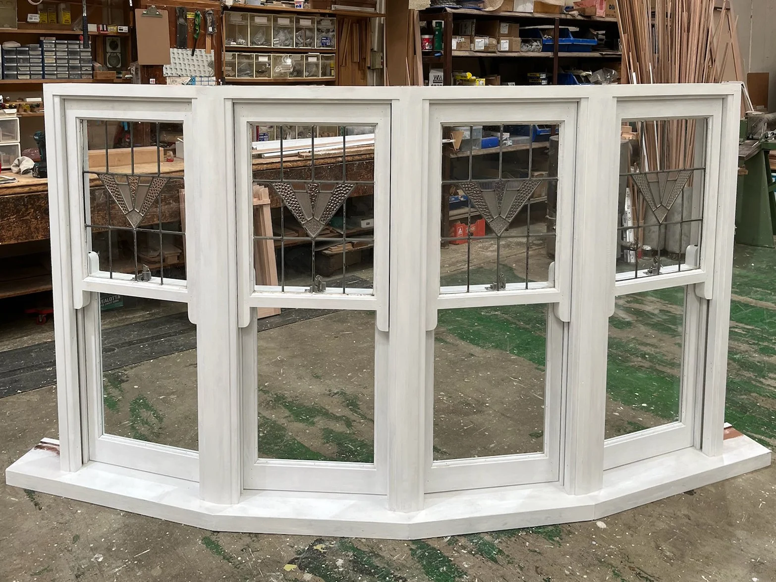 A white wooden window frame with four sections and decorative stained glass panels in a woodworking shop.