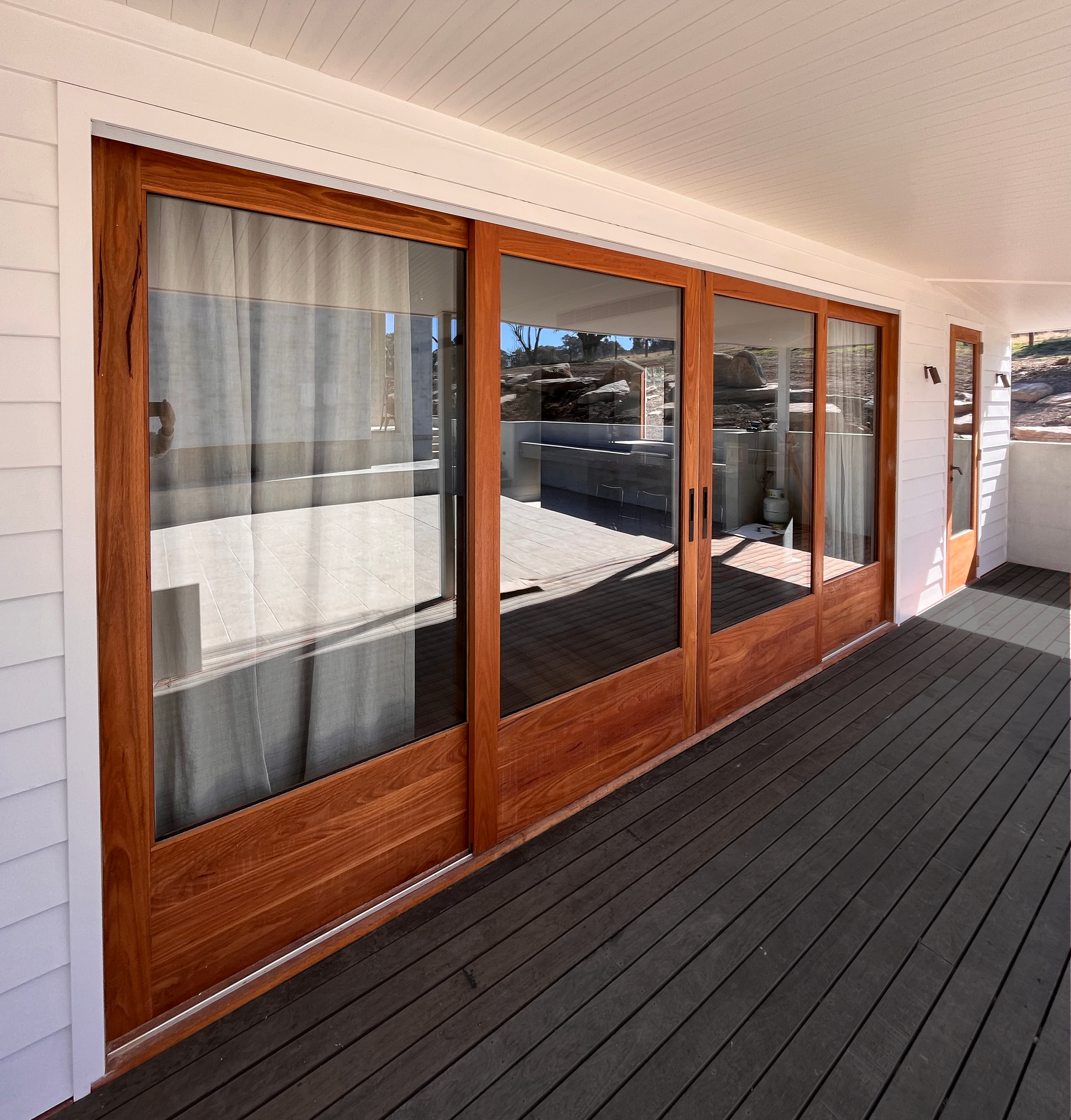 View of a house patio with wooden sliding glass doors, white siding, and a wooden deck.