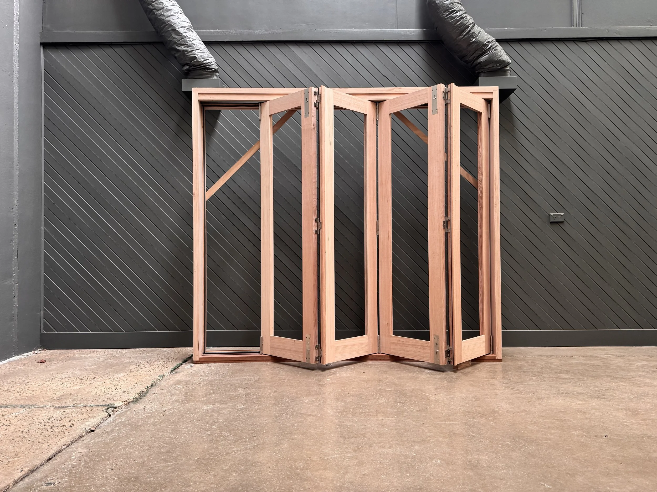 A wooden folding door partially opened in front of a black wall with diagonal lines.