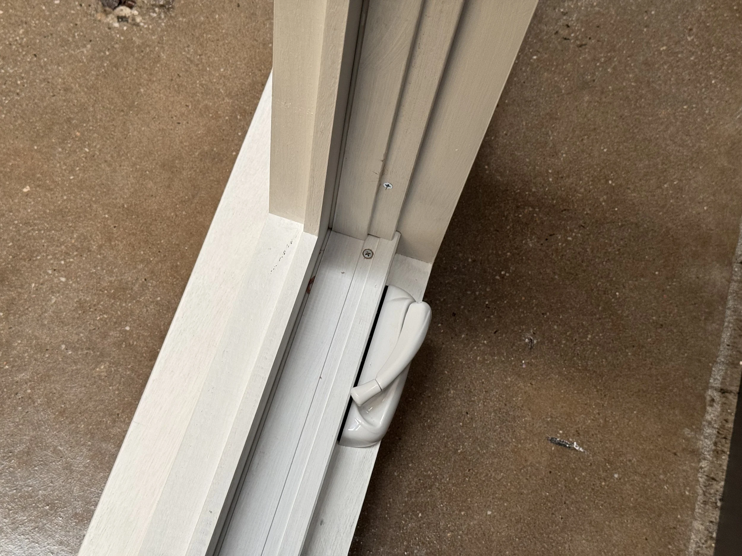 Close-up of a white sliding door track and a door handle on a white door, installed near a brown wall.