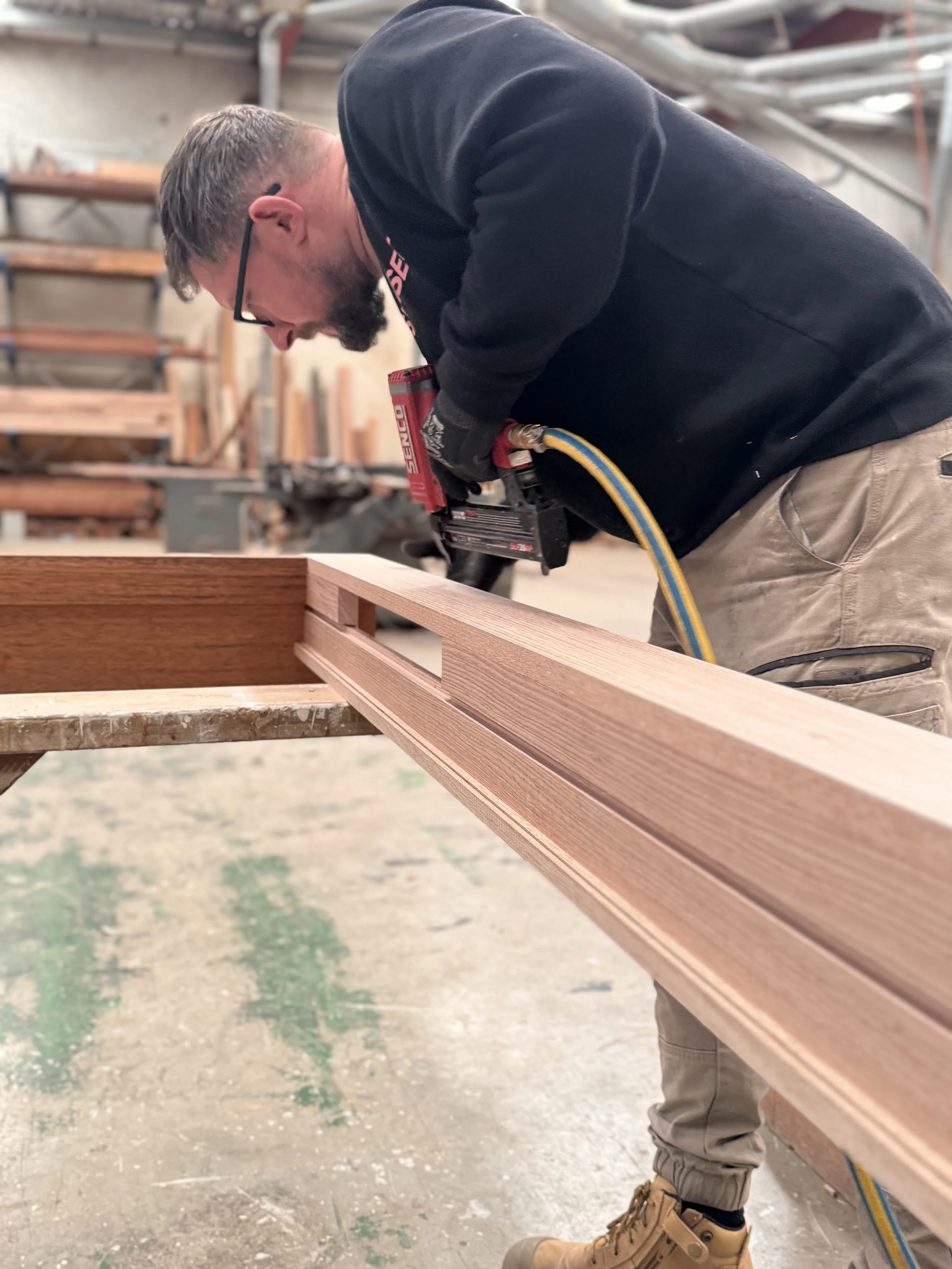 A man using a nail gun on a piece of wood in a workshop.